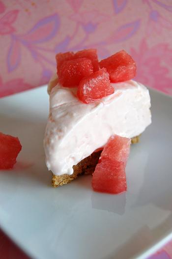 Slice of the watermelon cheesecake with watermelon fresca on top all on a white square plate with a pink floral background. 