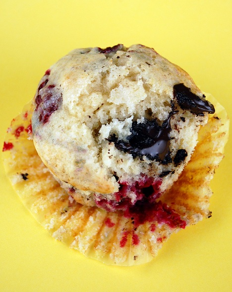 Raspberry Chocolate Almond Muffins with the muffin liner pulled away exposing the berries and chocolate in the muffin. Yellow background. 