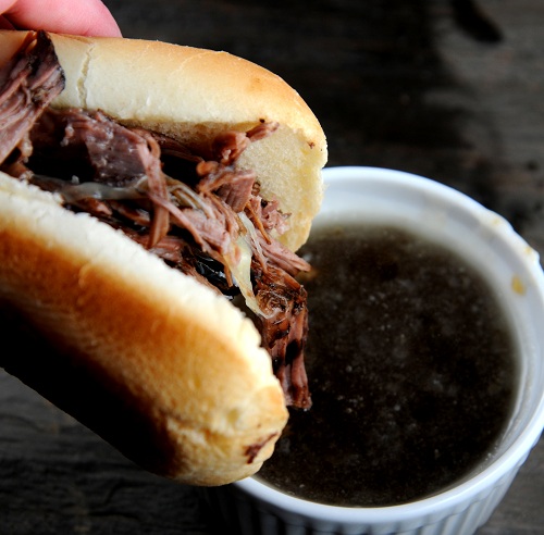 Person holding up the sandwich with the dip in a small white bowl in the background.