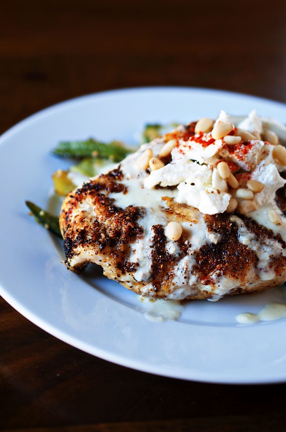 Side view of the chicken on a plate with the sauce, goat cheese, and pine nuts piled on top. 