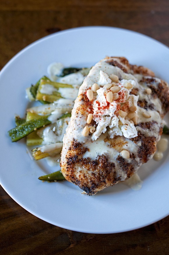 View of Tomatillo Beurre Blanc Chicken on a plate topped with goat cheese and pine nuts.