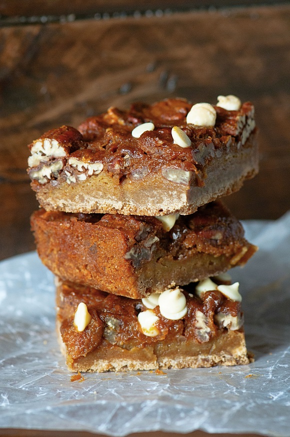 Three Pumpkin Pecan Pie Gingerbread Bars stacked up on parchment paper.