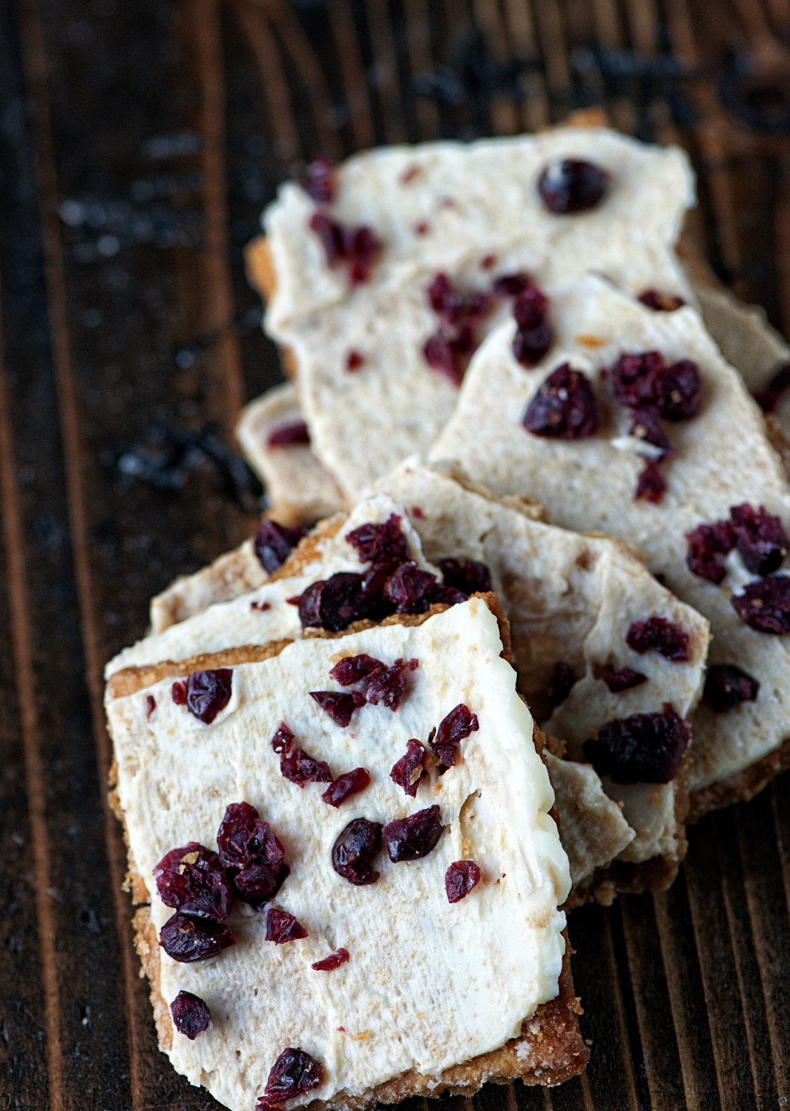 Stack of Cranberry Bliss Cracker Toffee fanned out with focus on the first cracker toffee piece. 