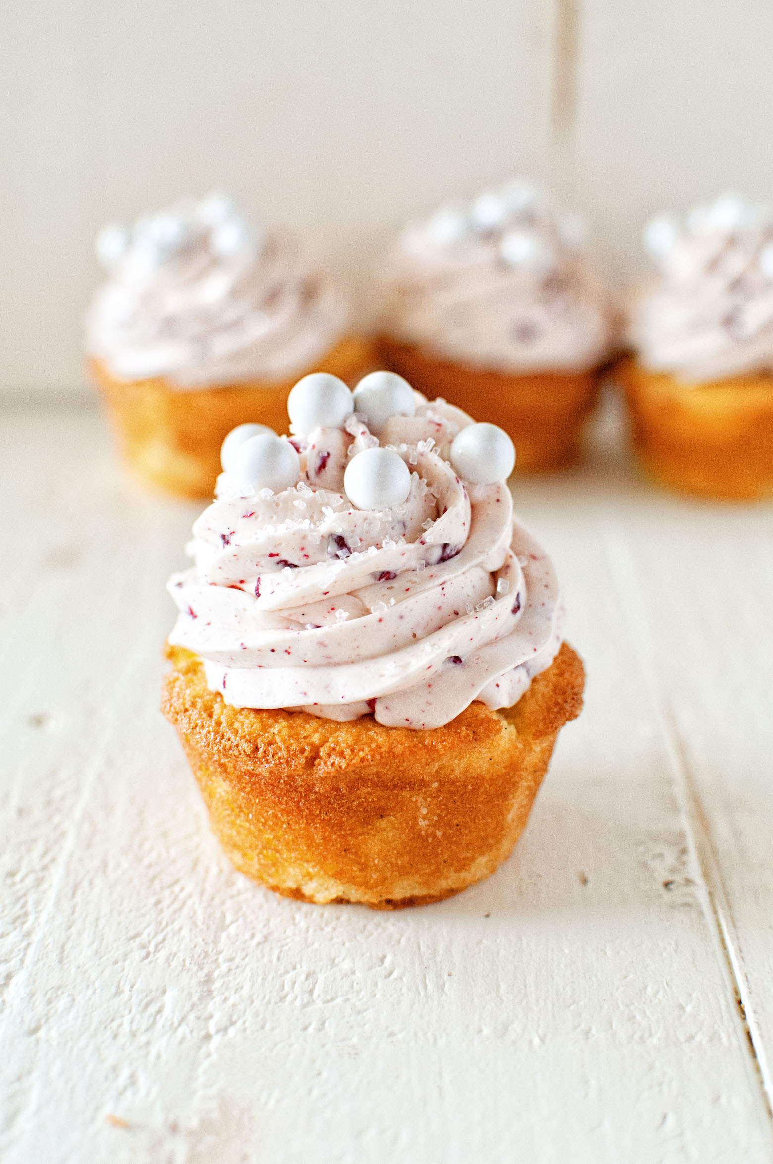 Side view of Raspberry Mimosa Cupcakes with one in front of a row of other cupcakes. 