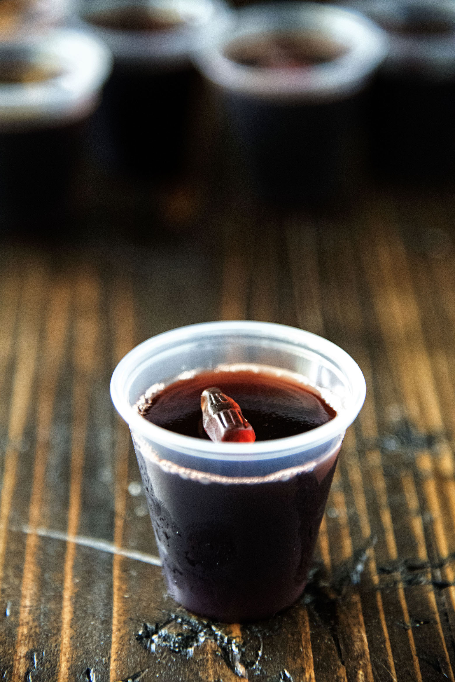 Single Black Cherry Spiced Rum and Coke Jell-O Shot with remaining shots in background.