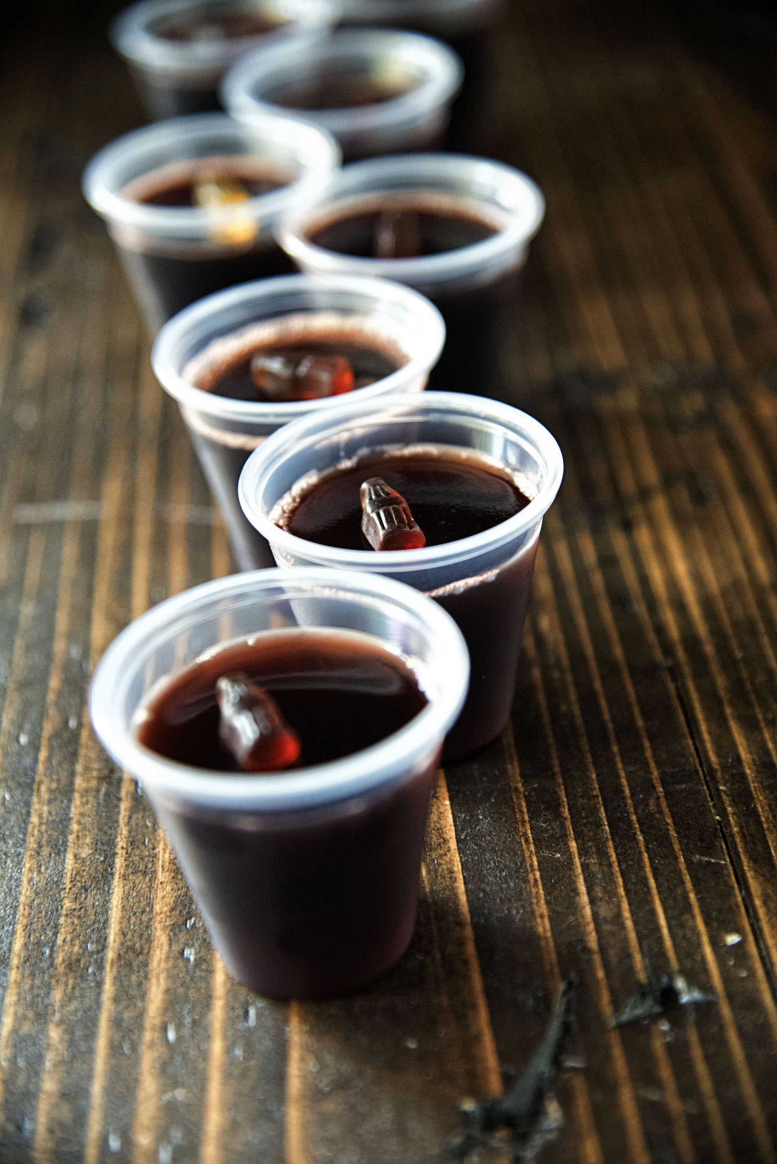 Black Cherry Spiced Rum and Coke Jell-O Shot all in a row with focus on the mini gummy cola.