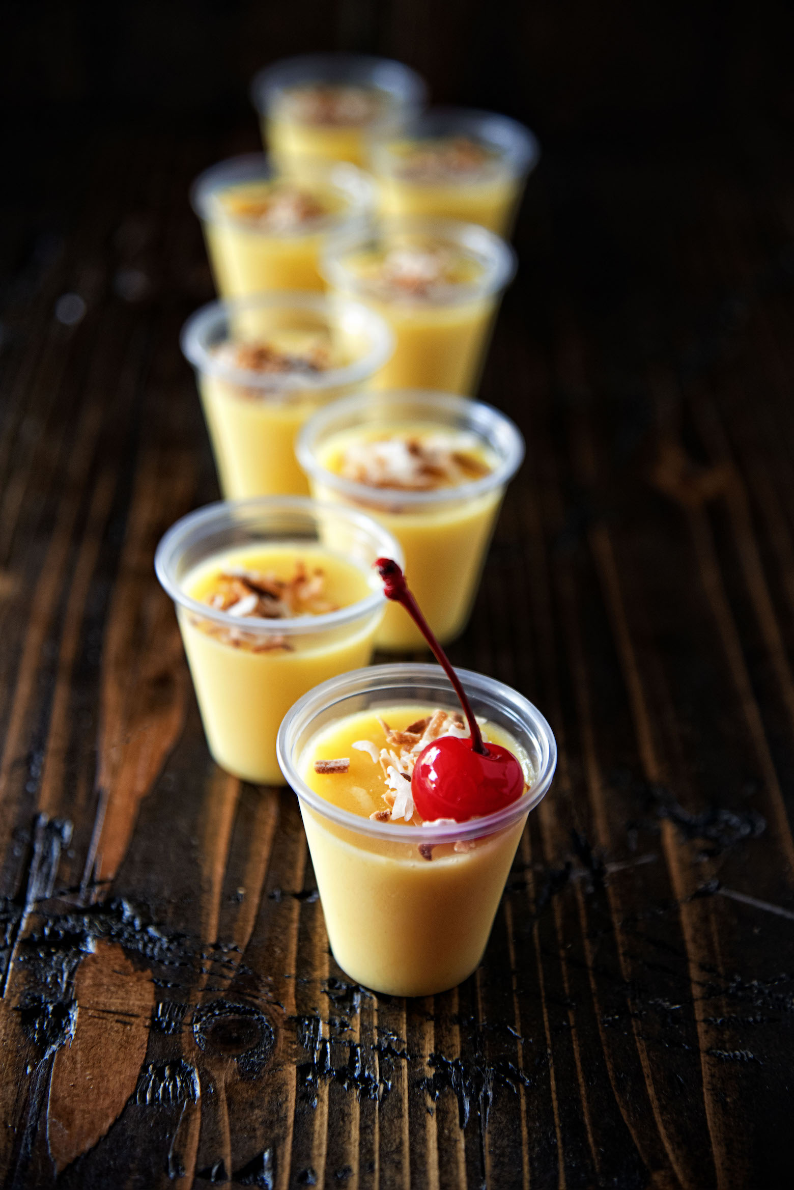 Pineapple Coconut Cream Jell-O Shots in a row with first shot having a cherry coming out of the shot. 