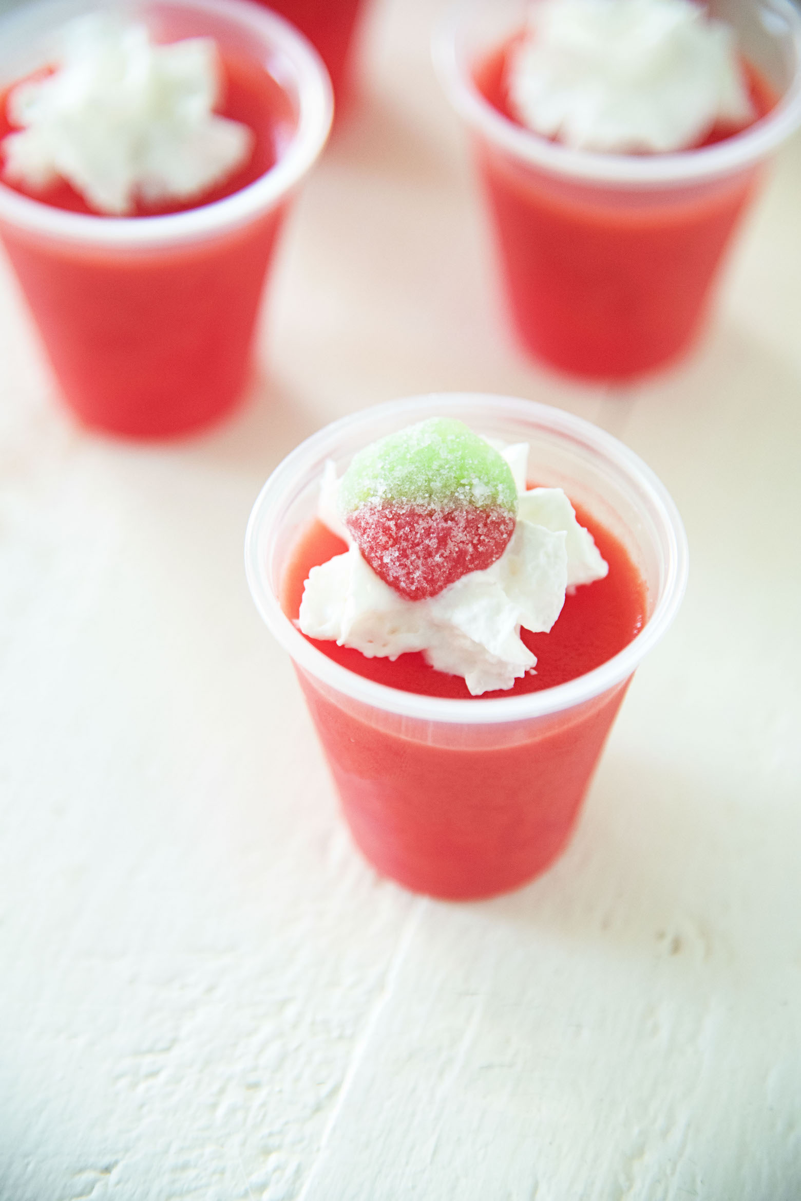 Three Strawberry Cream Jell-O Shots with whipped cream and gummy strawberry candy on top. 