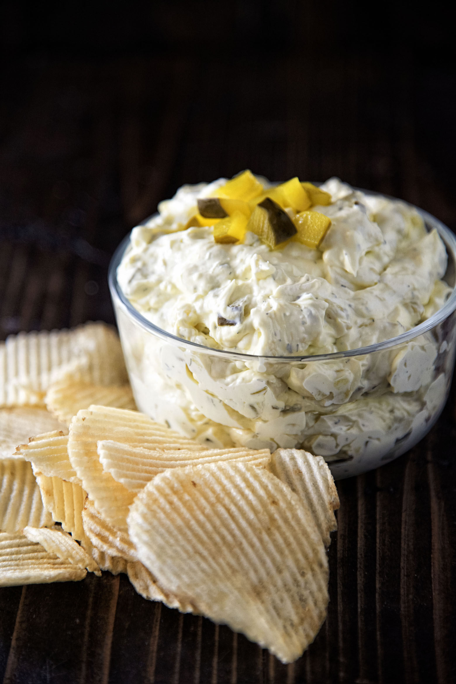 Side view of Cream Cheese Dill Pickle Dip in bowl with potato chips.