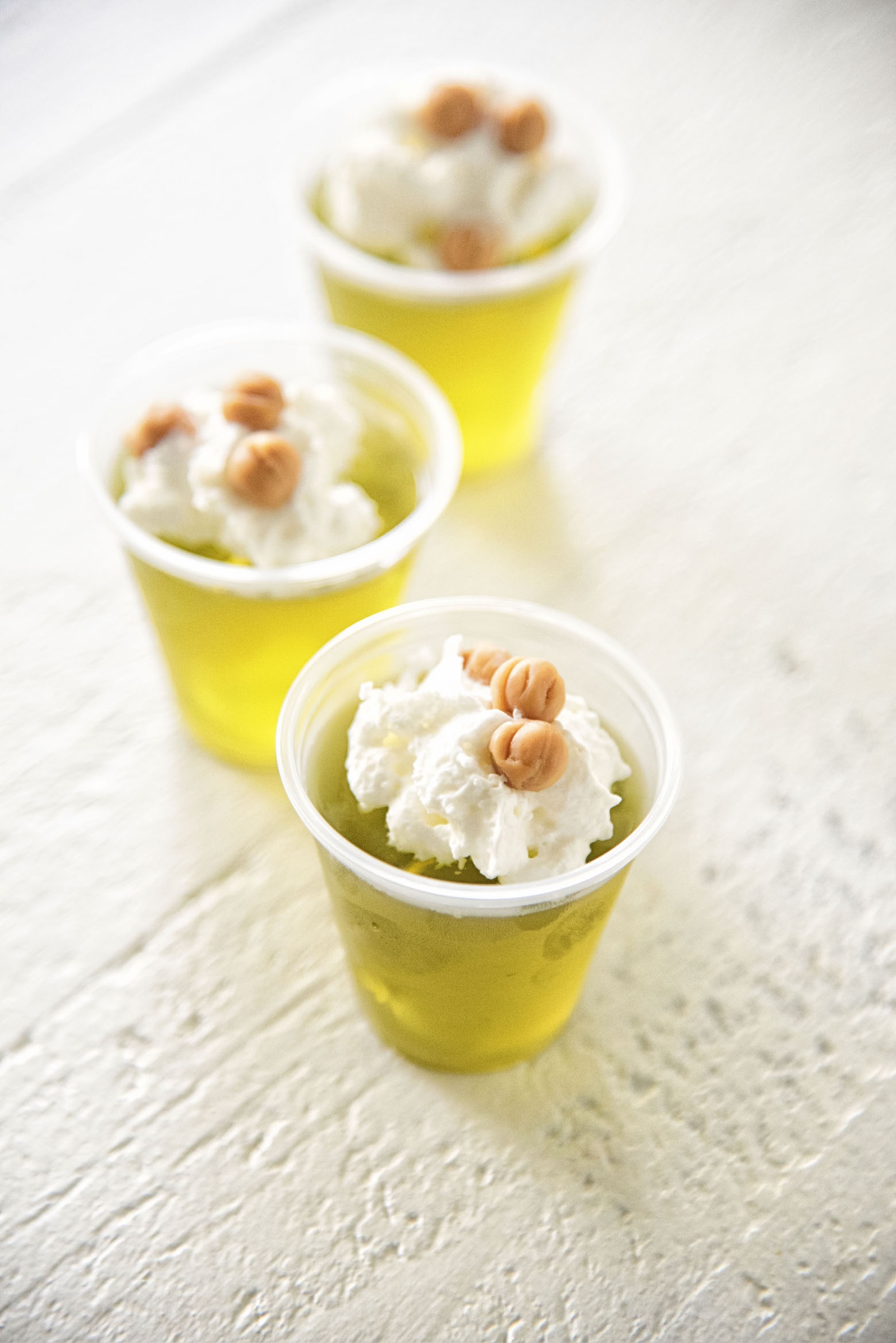 Three Salted Caramel Apple Whiskey Jell-O Shots in a row topped with whipped cream and caramel pieces. 