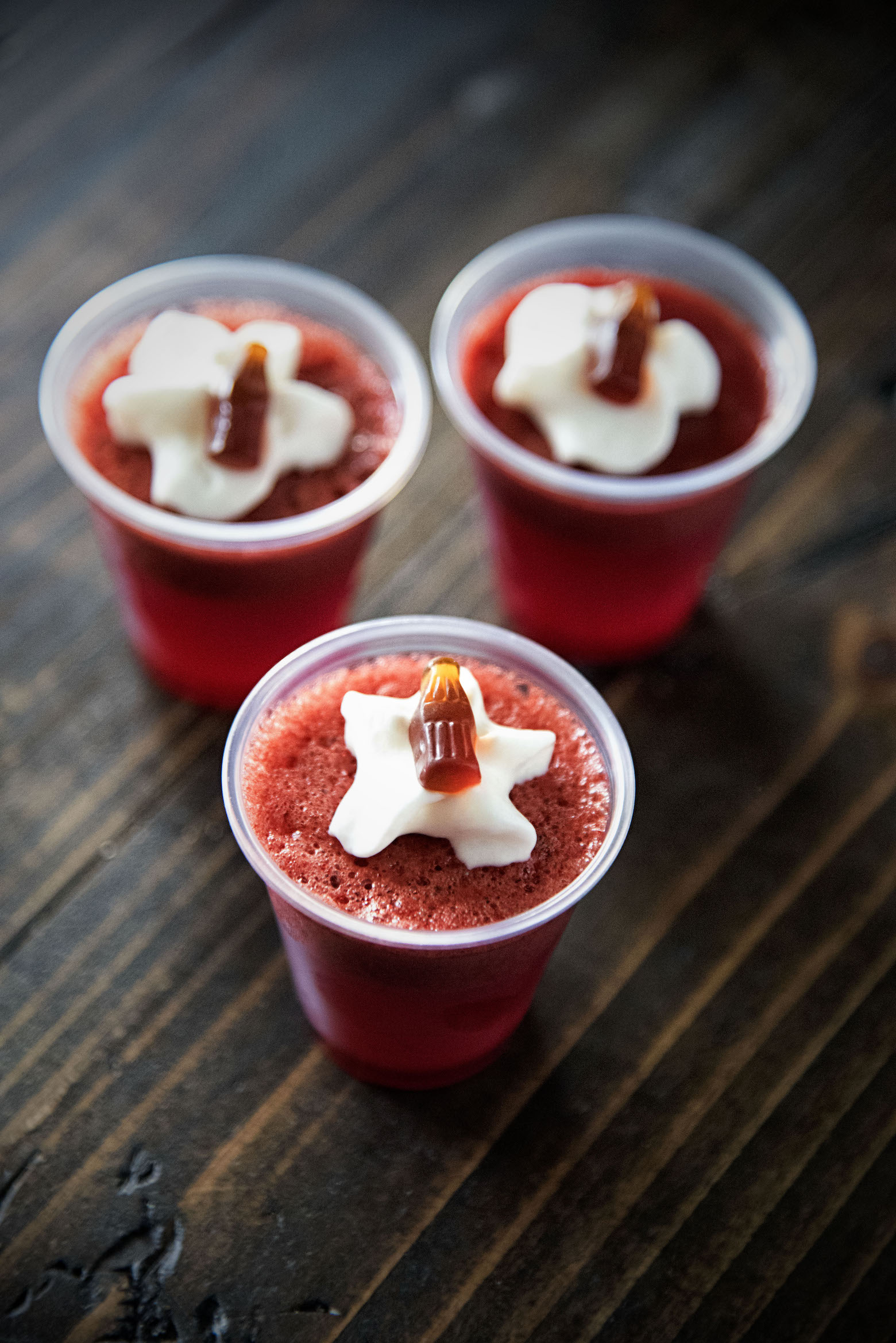 Three Cherry Cola Float Jello Shots with whipped cream and mini gummy colas.