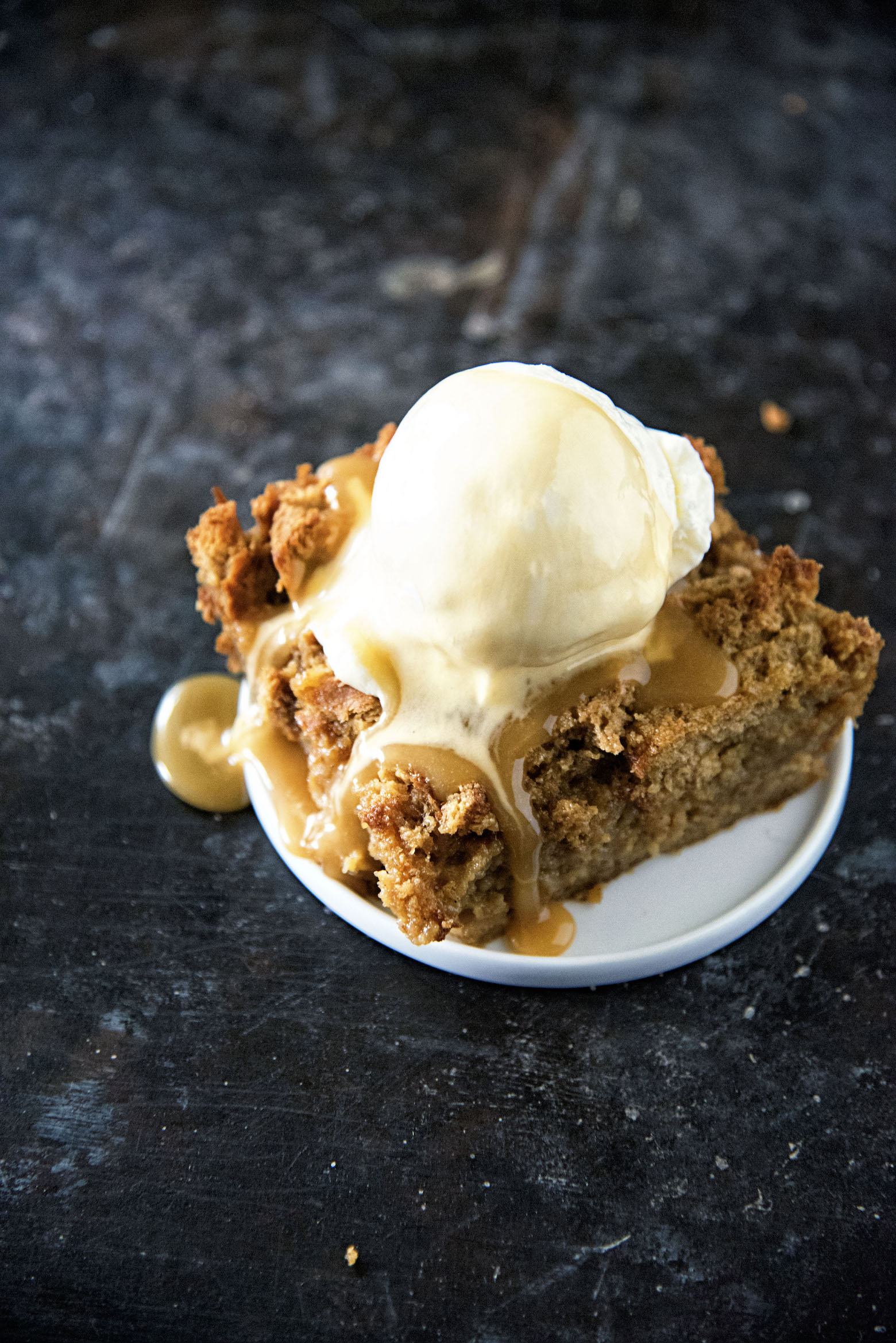 Slice of Gingerbread Bread Pudding with sauce and ice cream melting down on it. 
