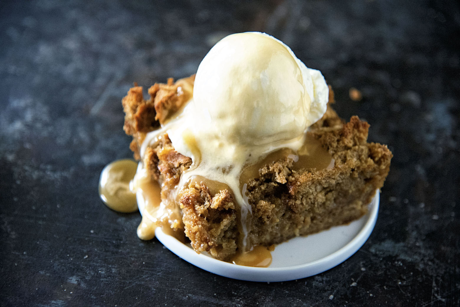 Side view of gingerbread bread pudding with sauce and ice cream dripping down.