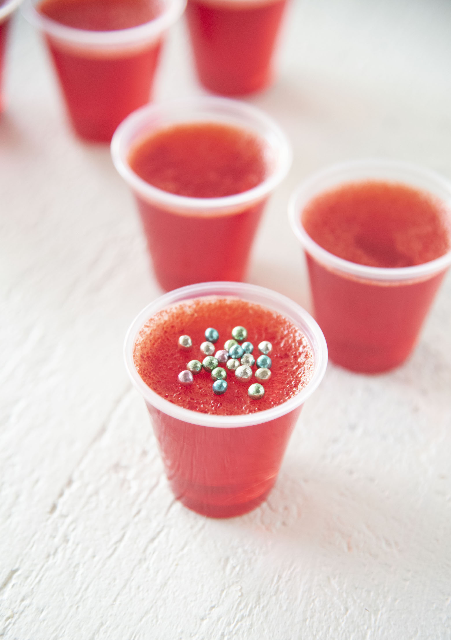 Several Raspberry Peach Bellini Jello Shots with first shot being in focus with colorful sprinkles on it.