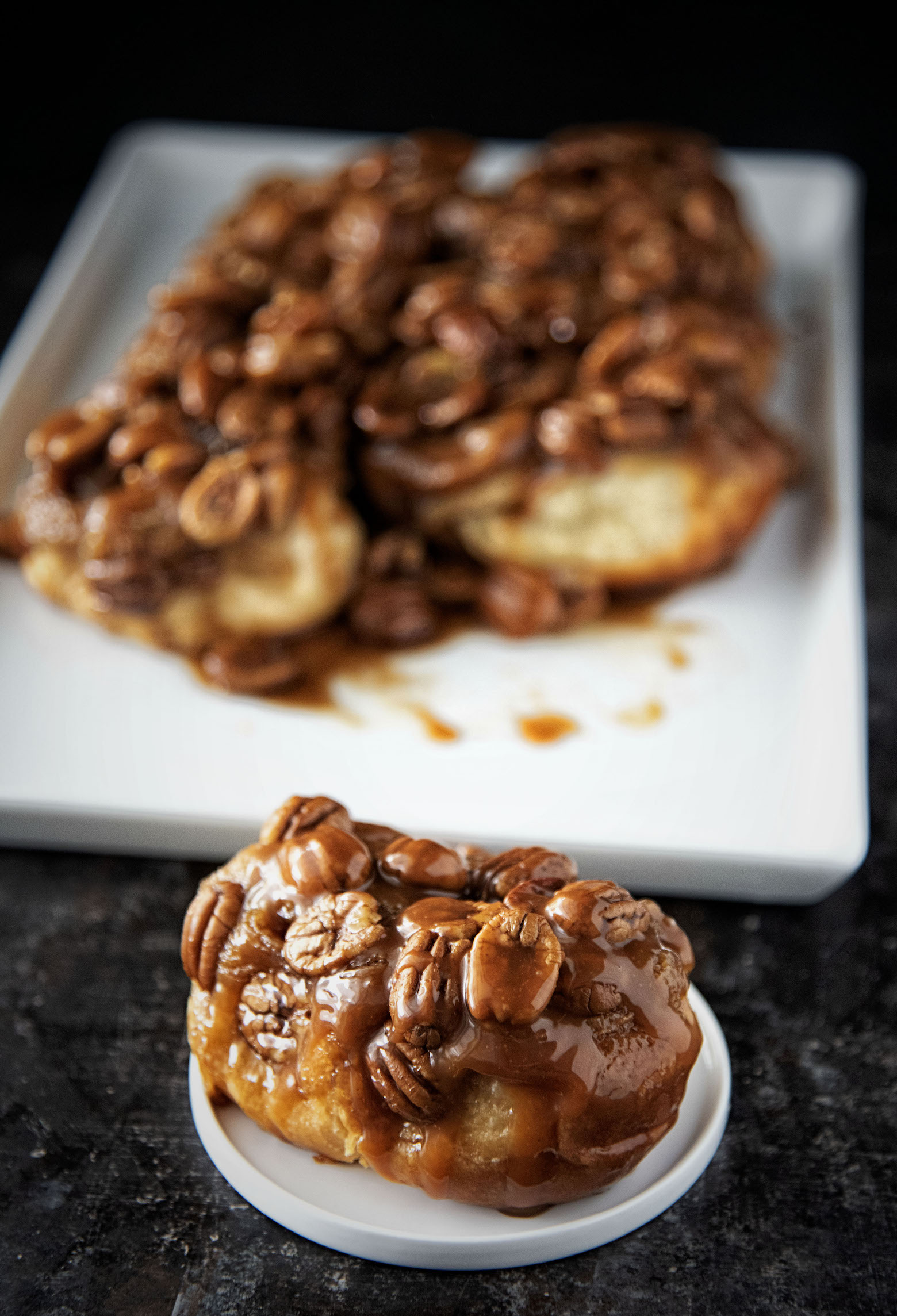 Close up of a Whiskey Butterscotch Pecan Sticky Bun with the remaining buns in the background.