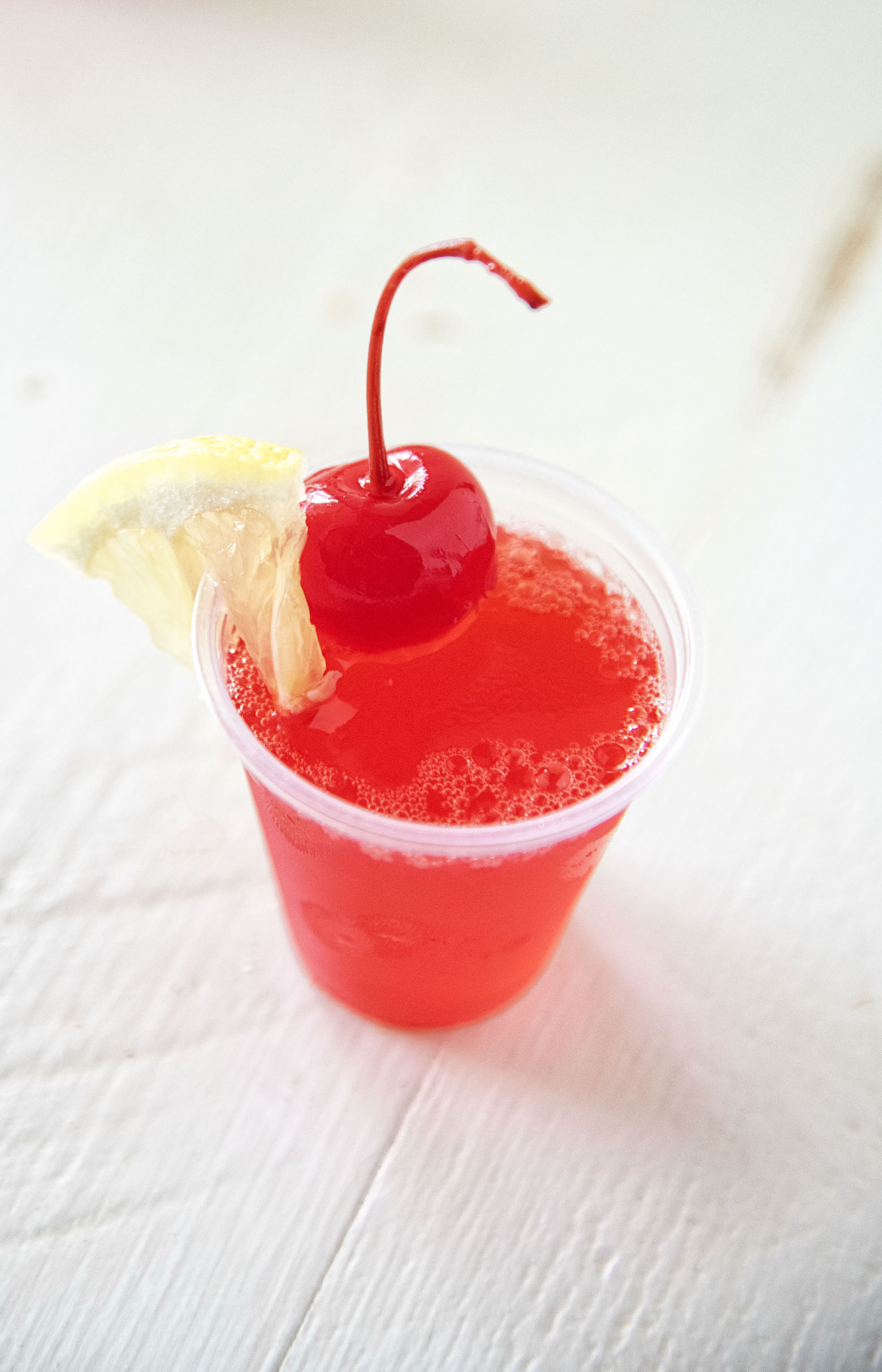 Single shot Cherry Lemonade Jello Shot with lemon wedge and cherry on top. 