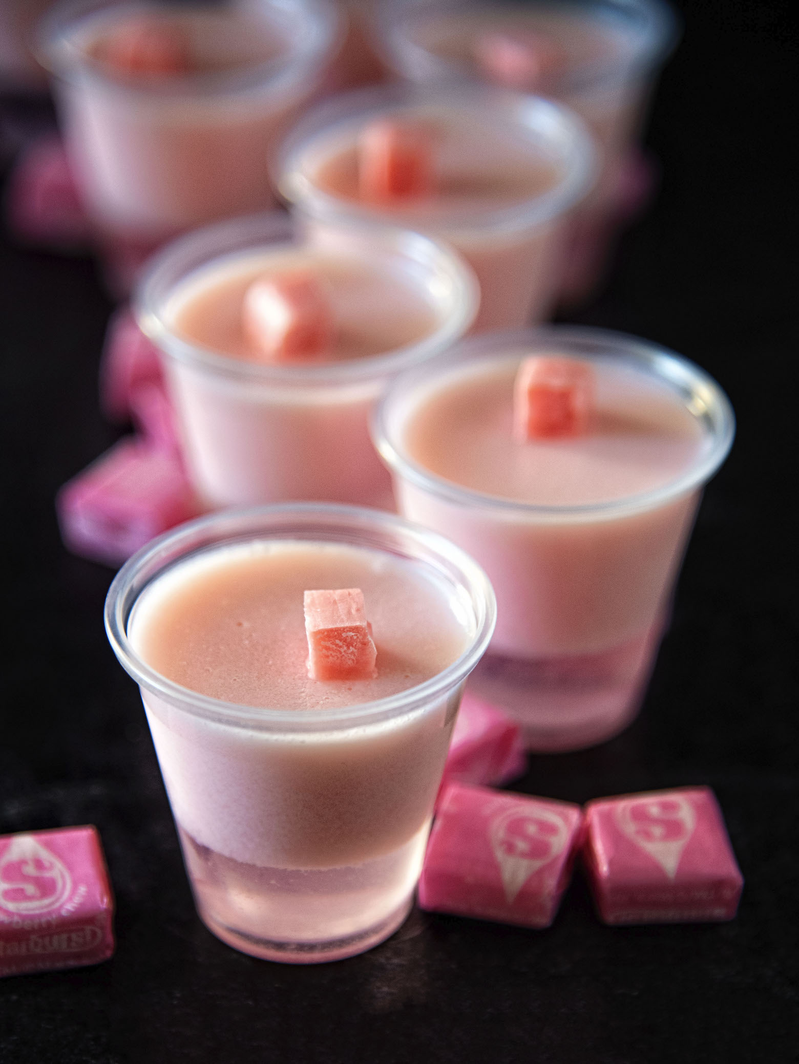 Pink Starburst Jell-O Shots in a row with focus being on the first shot.