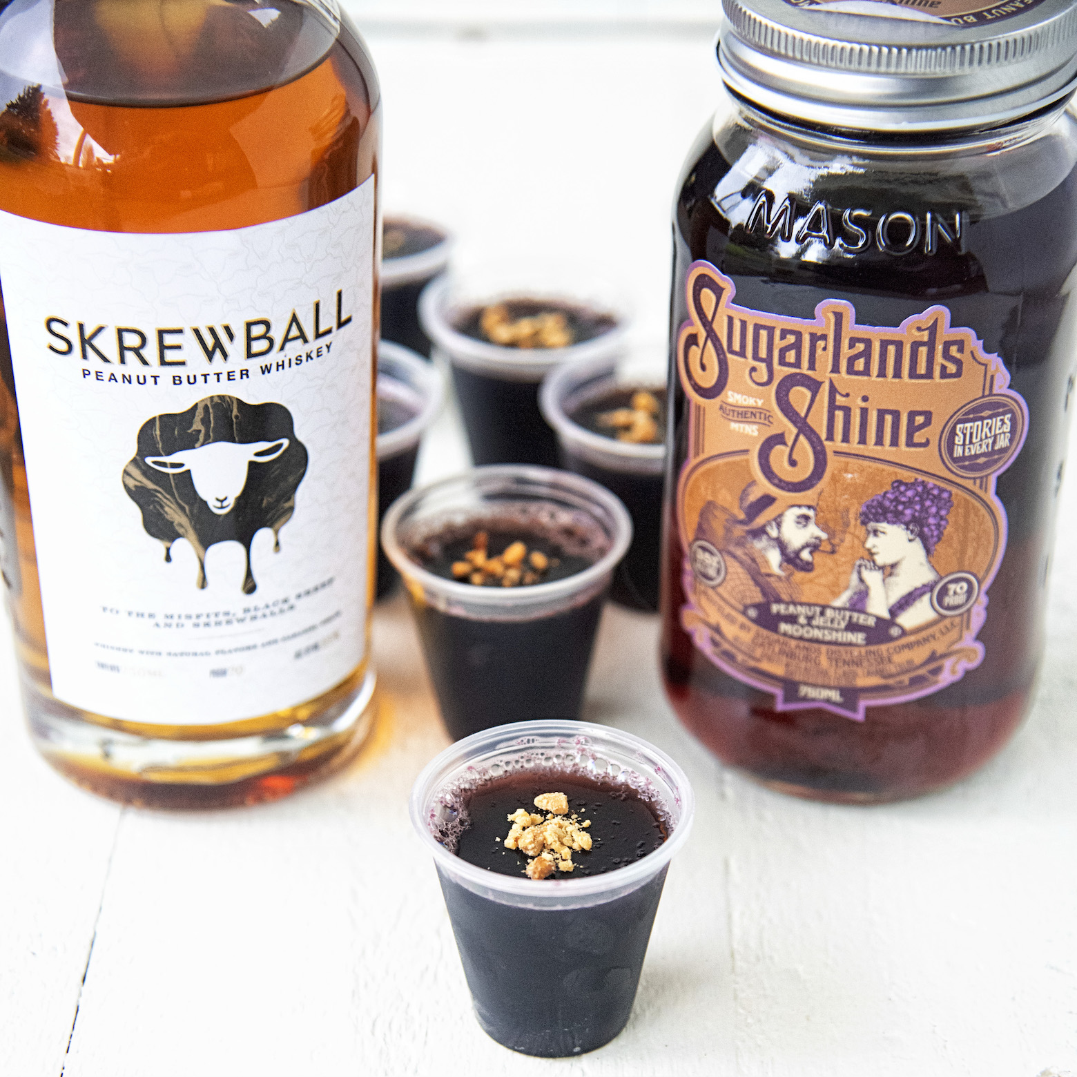 Peanut Butter Grape Jelly Jello Shots with Peanut Butter and Jelly Moonshine bottle on one side and Skrewball Peanut Butter Whiskey on the other side of the jello shots. 