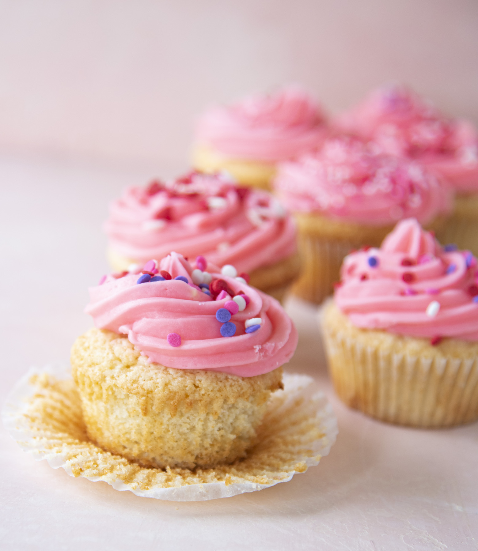 Side view of Pink Vanilla-Vanilla Cupcakes with one unwrapped