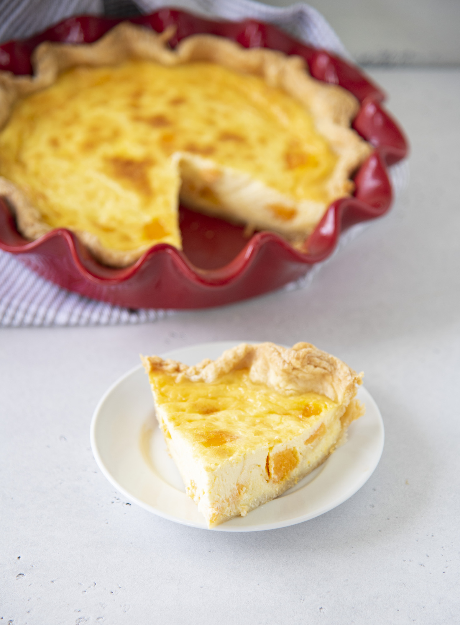 A slice of Vegetarian Triple Cheddar Quiche on a plate with the remainder of the quiche in the background. 