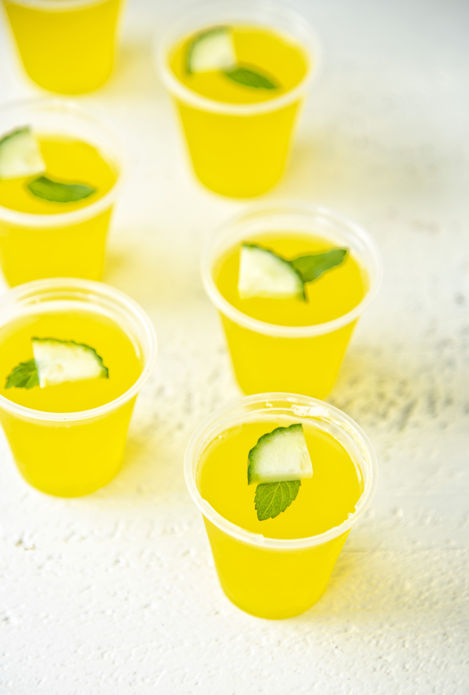 Several Cucumber Mint Lemonade Jello Shots with mint and cucumber garnish. Part of the Best Jello Shot Recipes rondup. 