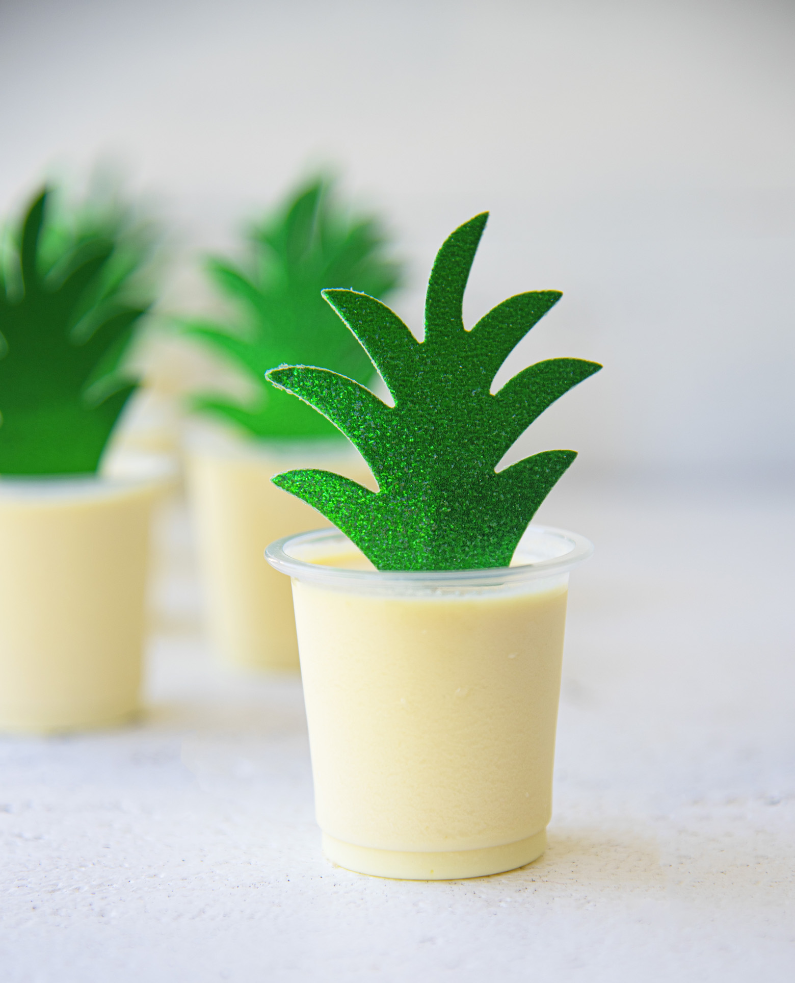 Dole Whip Pineapple Jello Shots are part of the Best Jello Shot Recipes Round up. This photo has the yellow Dole Whip shots with a sparkly leaf coming up out of it. 