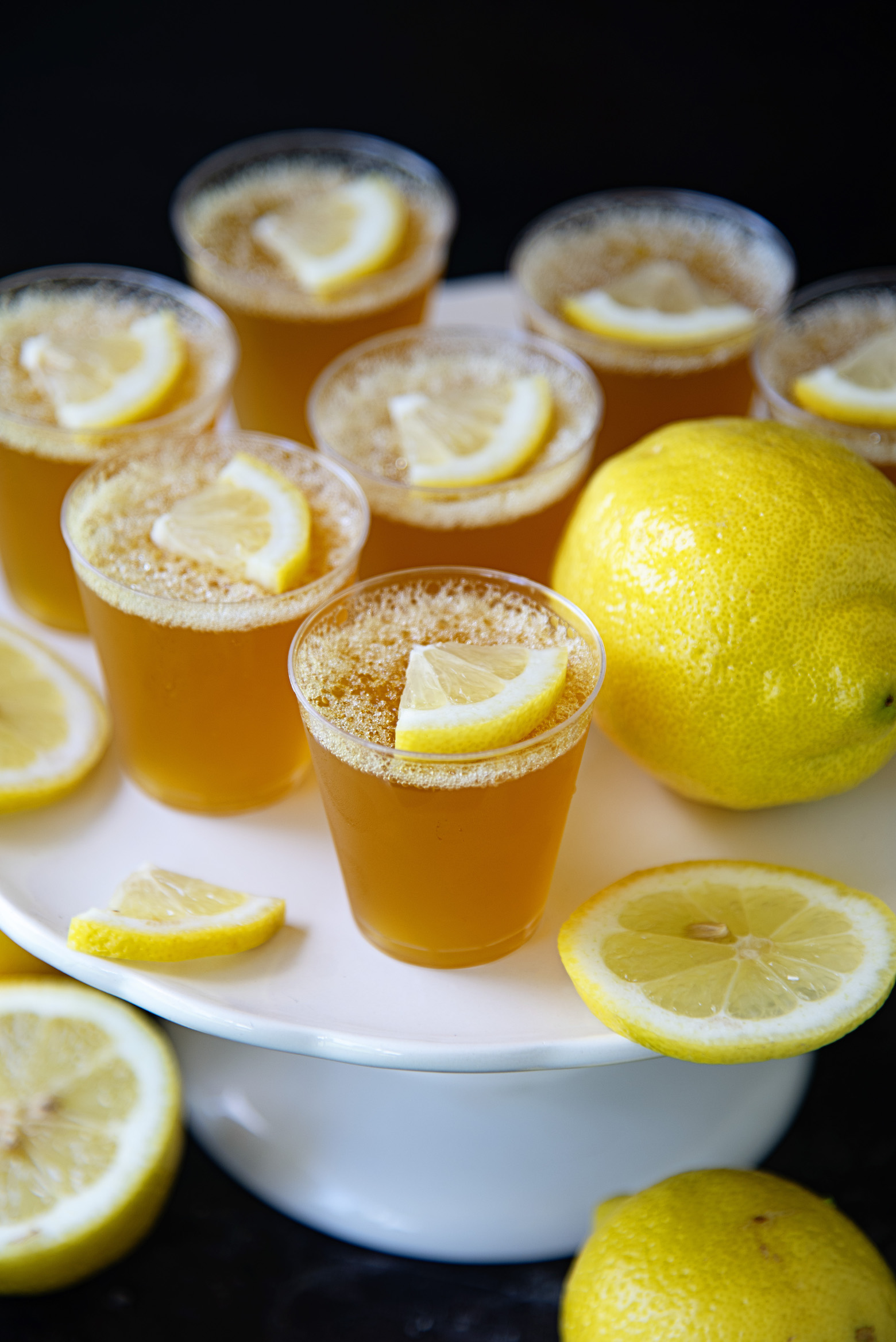 Several Boozy Arnold Palmer Jello Shots on a platter next to a whole lemon and some cut lemon. 