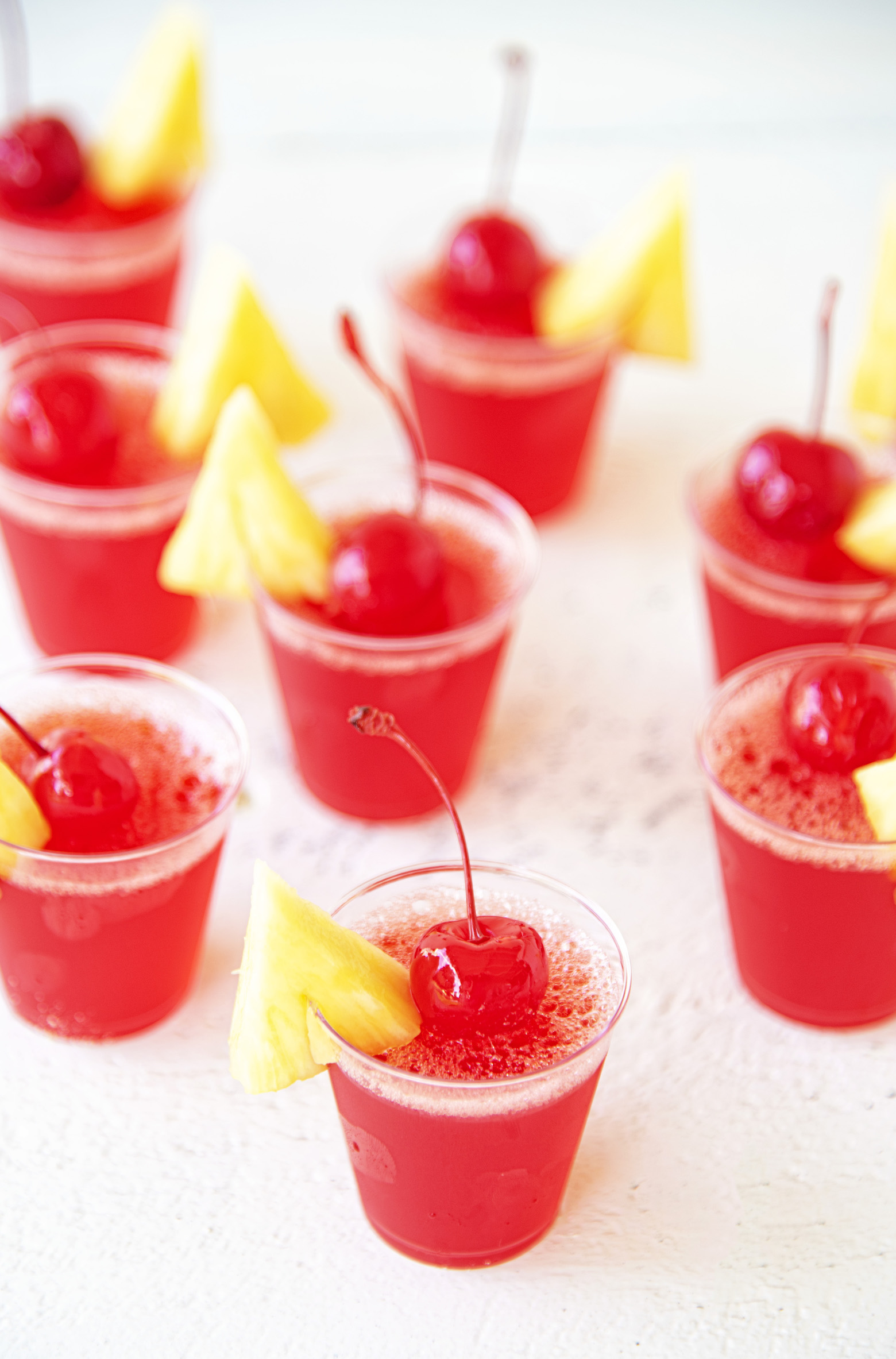 Fruit Punch Moonshine Jello Shots clustered together with cherries and fresh pineapple on top. 
