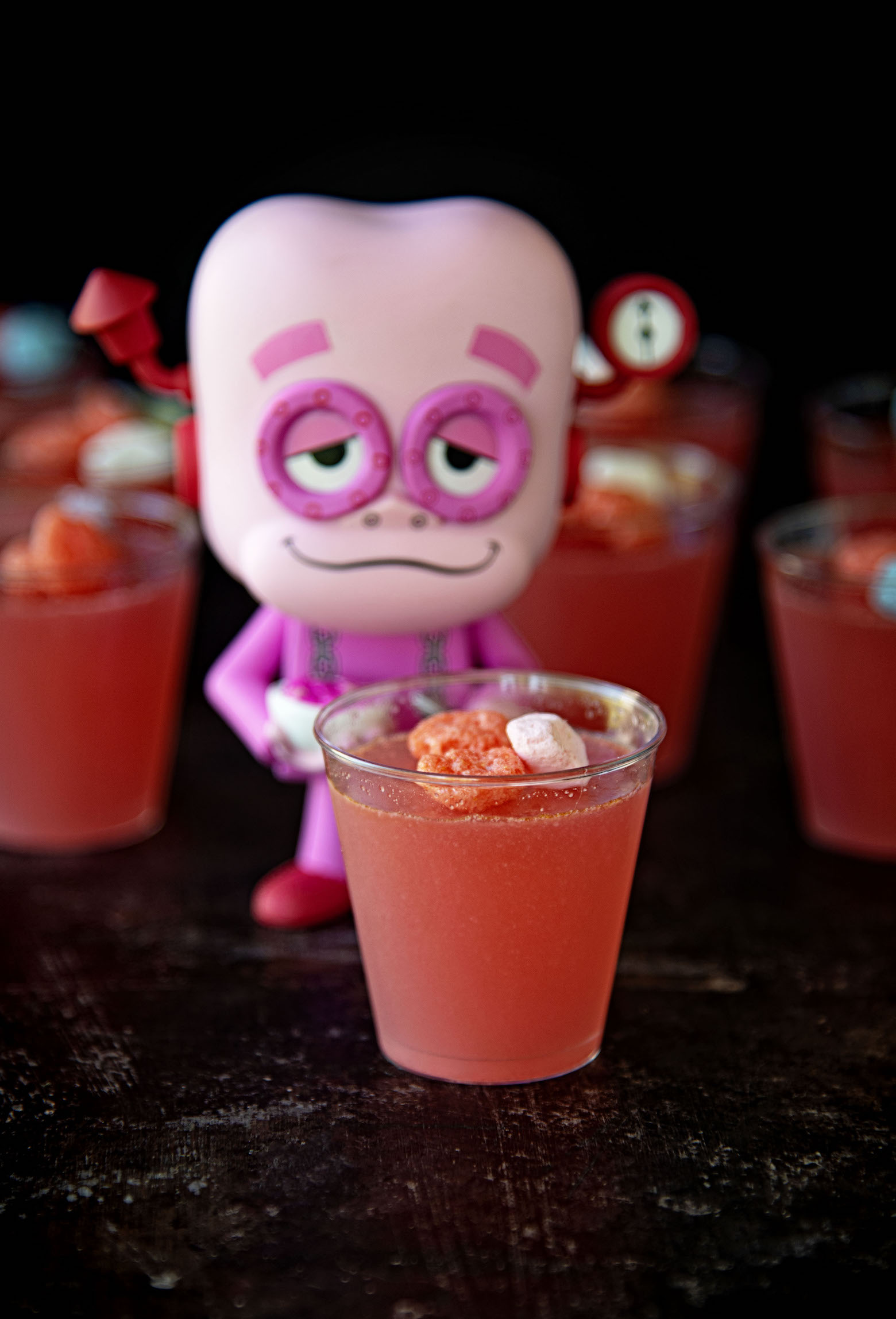 Franken Berry standing behind a jello shot with more jello shots behind him.