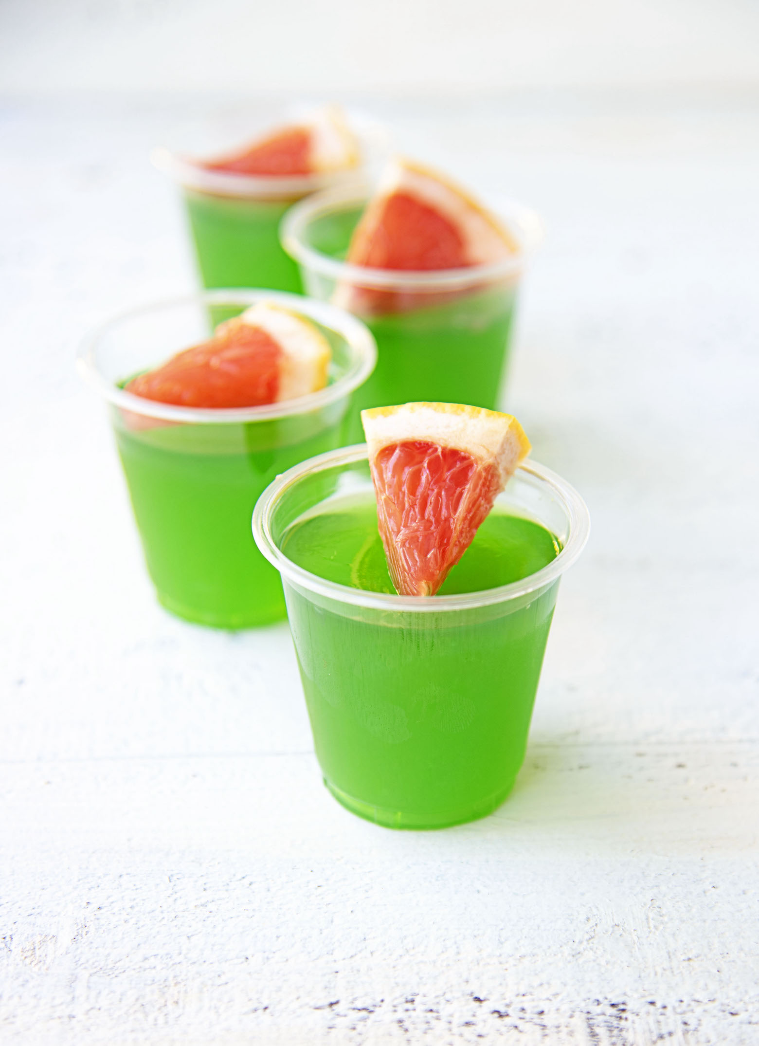Paloma Jello Shots in a row with focus being on the first shot. All shots have a piece of grapefruit on them. Part of the Best Jello Shot Recipes round up.