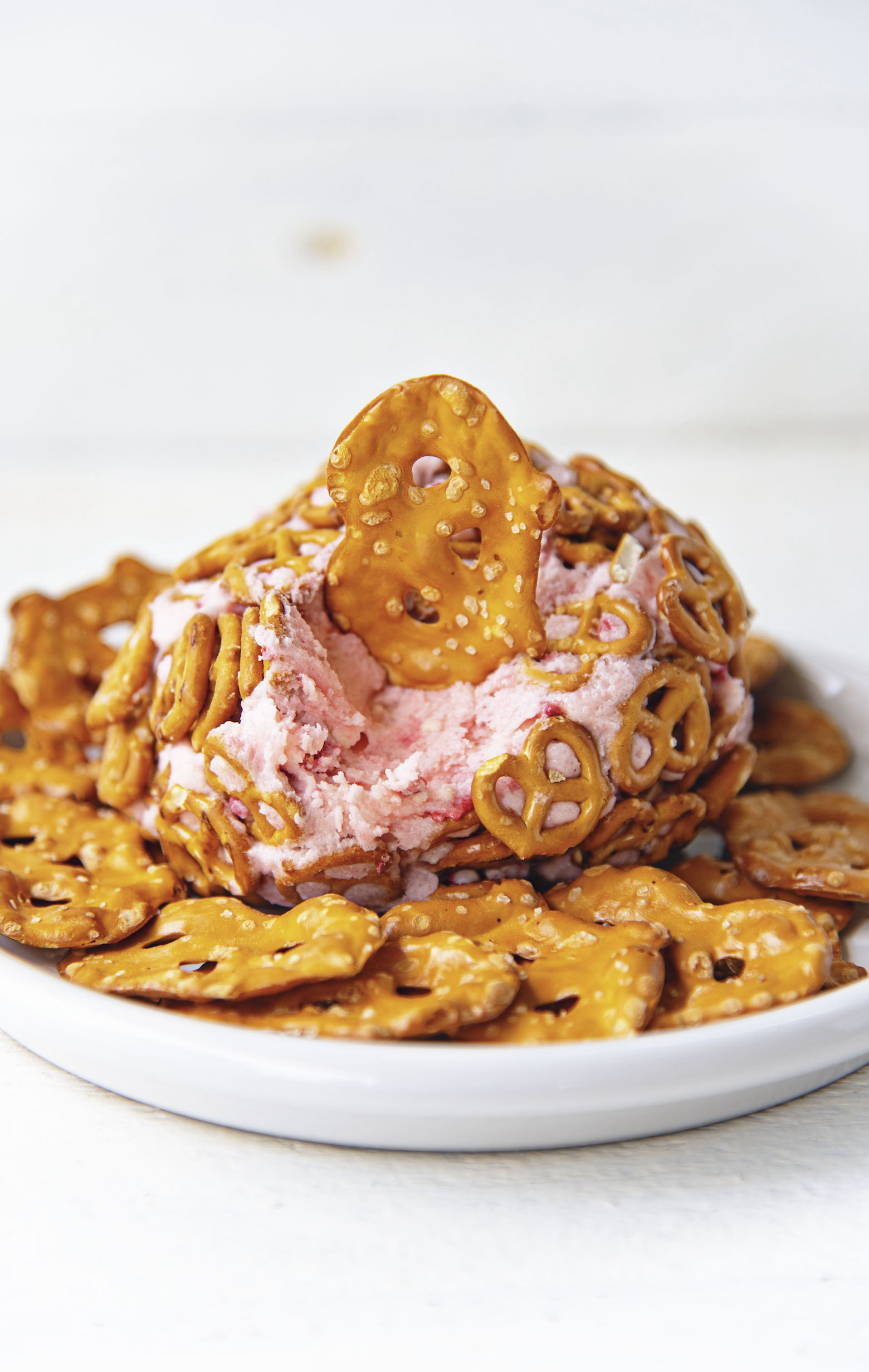 View of Strawberry Pretzel Cheesecake Cheese Ball with pretzel dipped in it