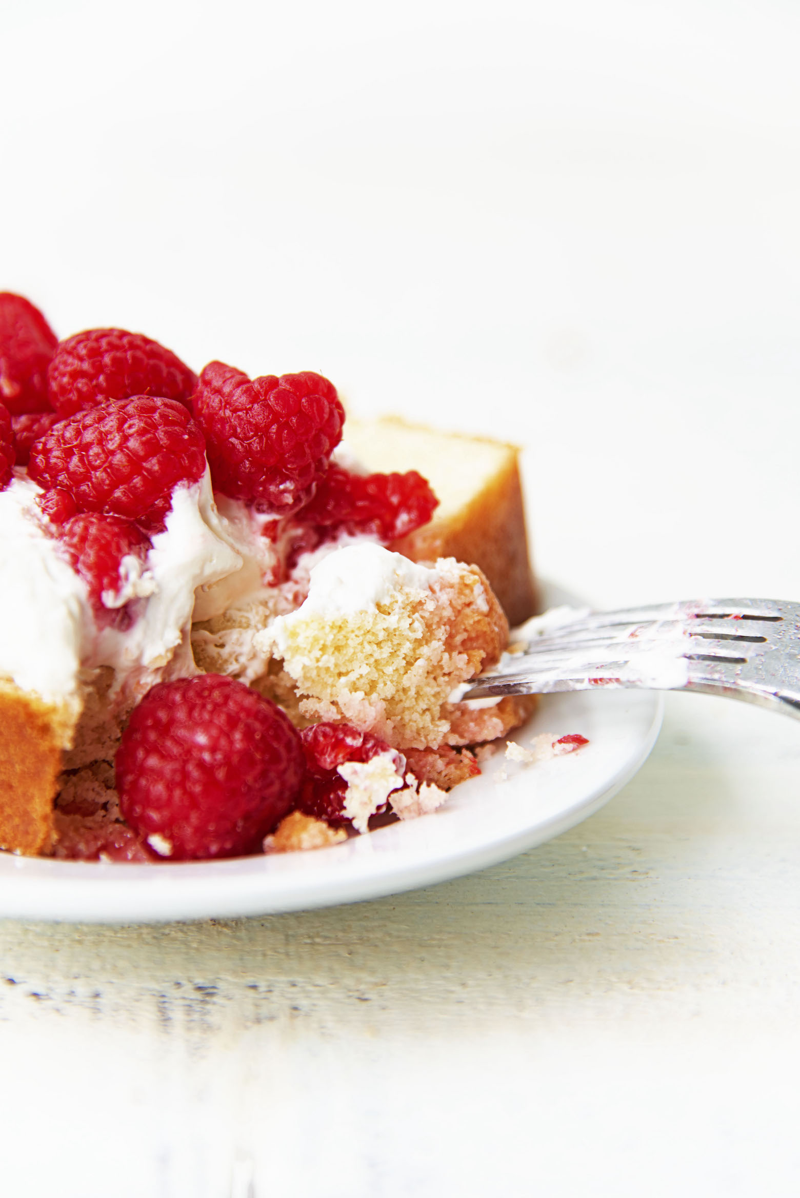 Vanilla Butter Loaf Cake with whipped cream and berries with a fork taking out a bite.