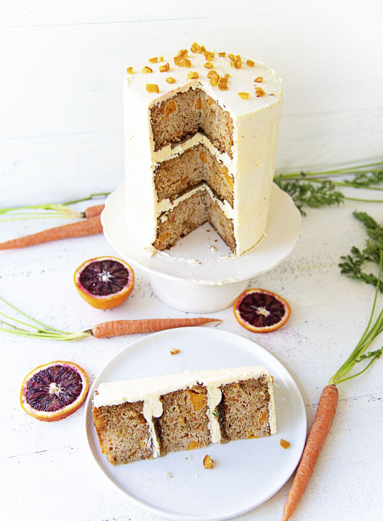 Slice of Citrus Sunshine Carrot Cake on plate with remaining cake on a cake plate in the background. 