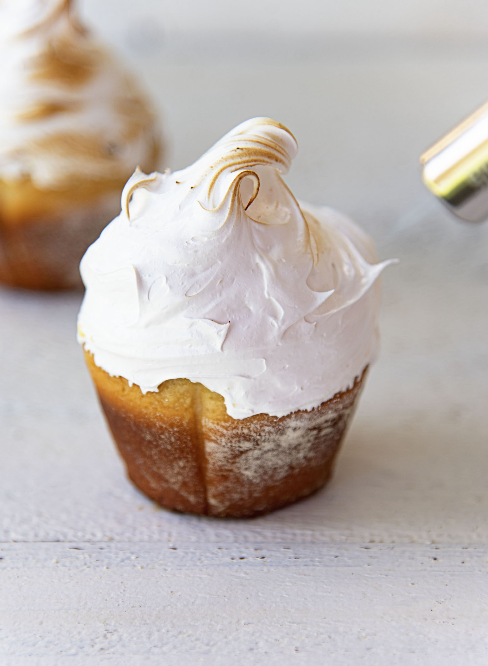 Picture of meringue covered sweet roll with blowtorch toasting the meringue. 