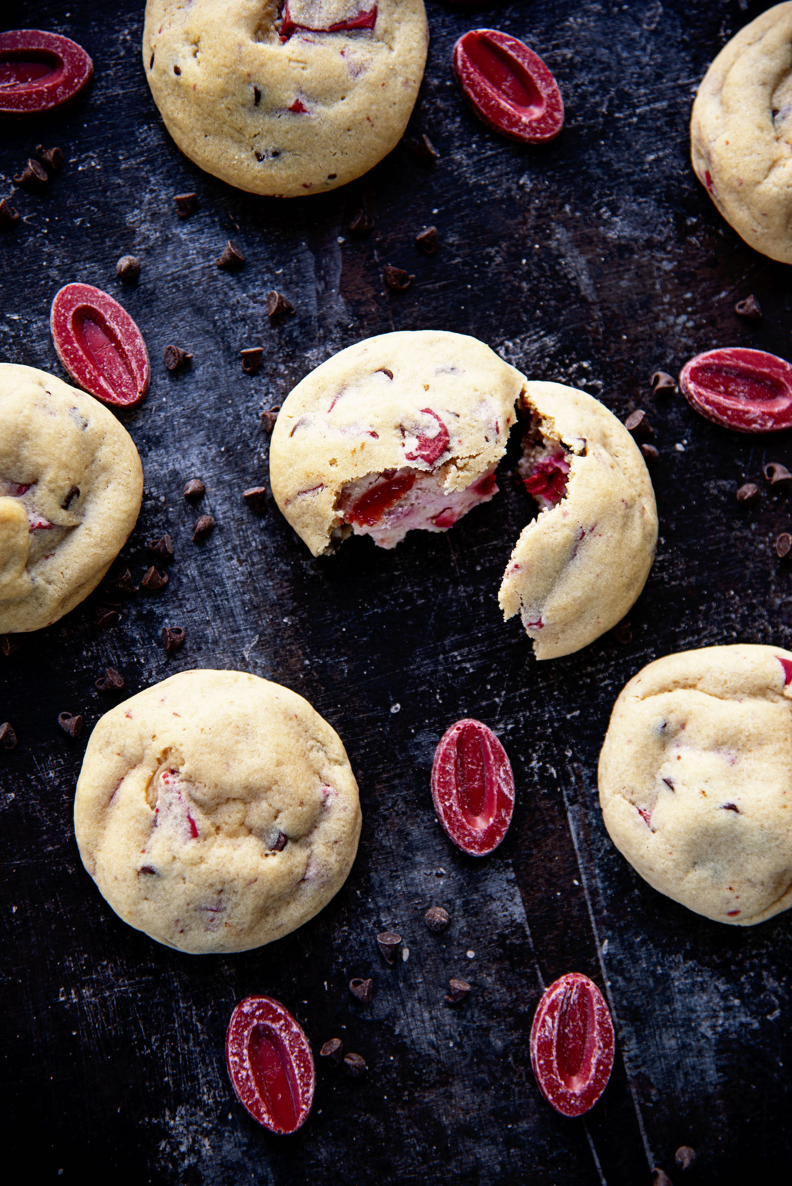 Overhead shot of 6 cookies. One cookie in the middle is split open showing the strawberry cheesecake filling. 