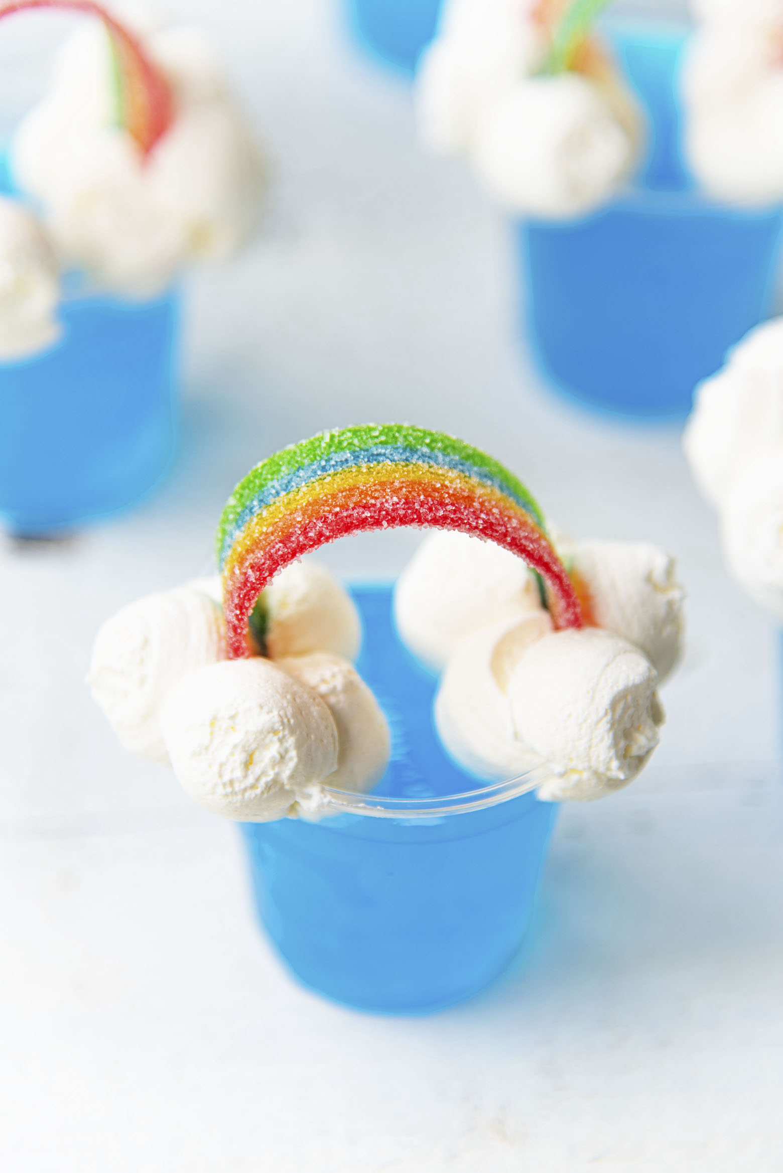 Close up of Blue Hawaiian Rainbow Jello Shot with focus on the candy rainbow and whipped cream clouds. Part of the Best Jello Shot Recipes. 