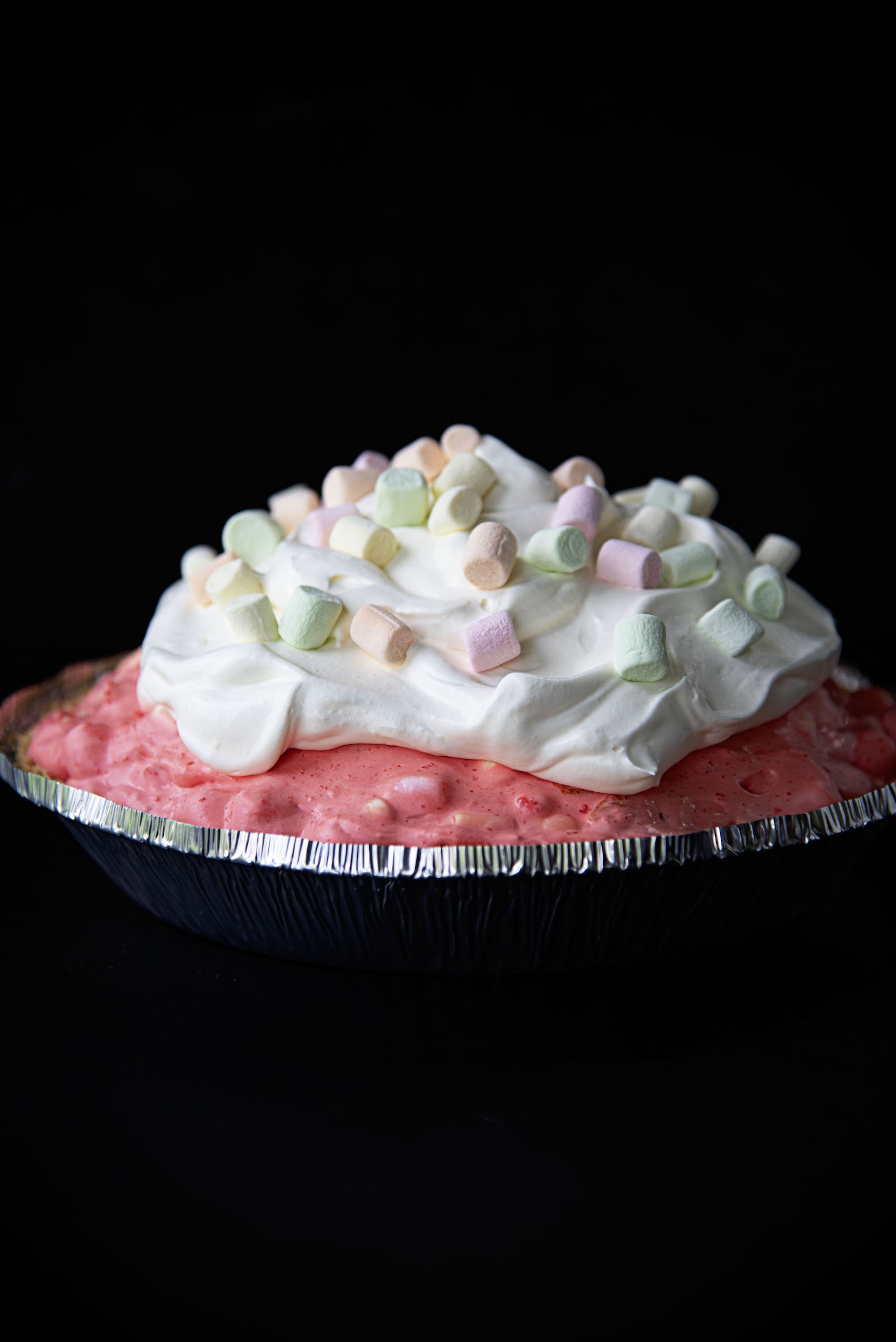 Side view of Fruity Marshmallow Raspberry Jello Pie with dark background.
