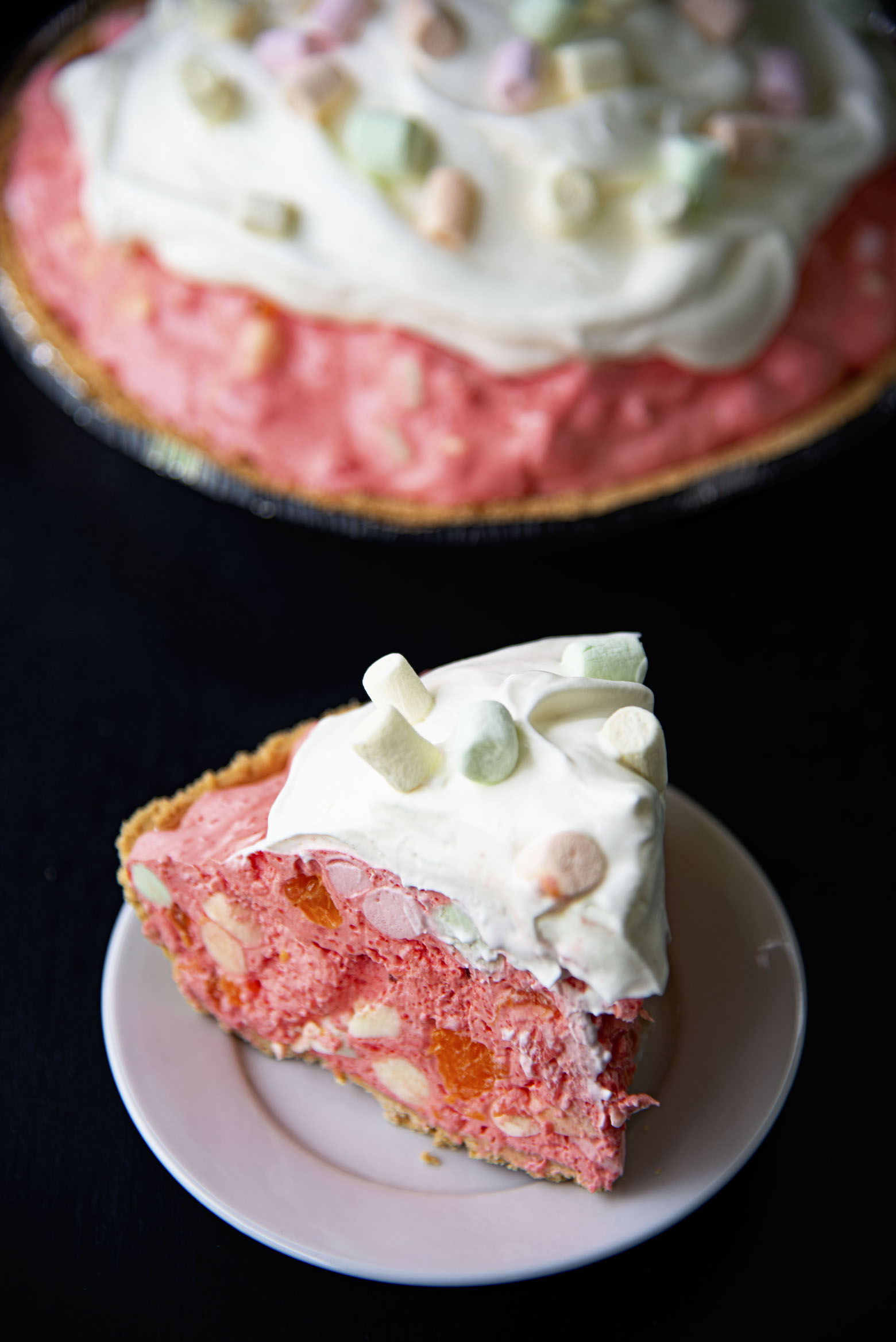 Piece of Fruity Marshmallow Raspberry Jello Pie on a plate in front of remaining pie. 