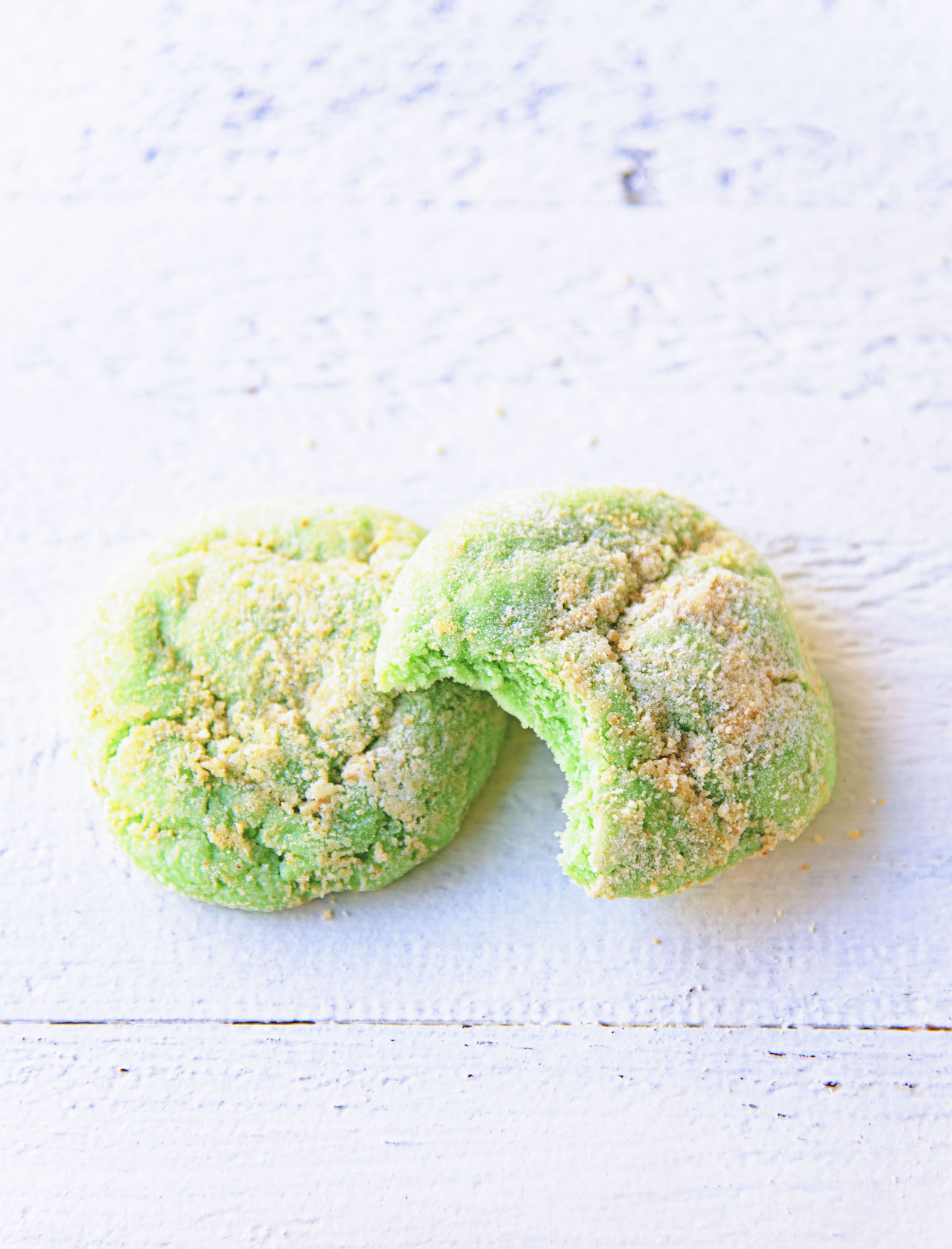 Overhead shot of two Key Lime Pie Crinkle Cookies one with bite out of it. 