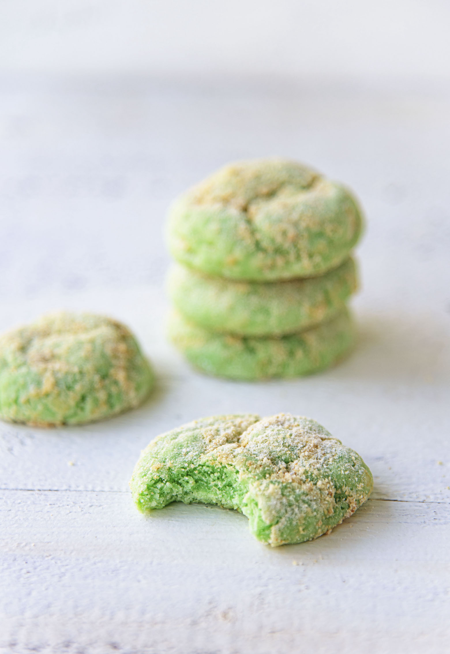 Key Lime Pie Crinkle Cookies stacked three up with a cookie up front with a bite taken out. 