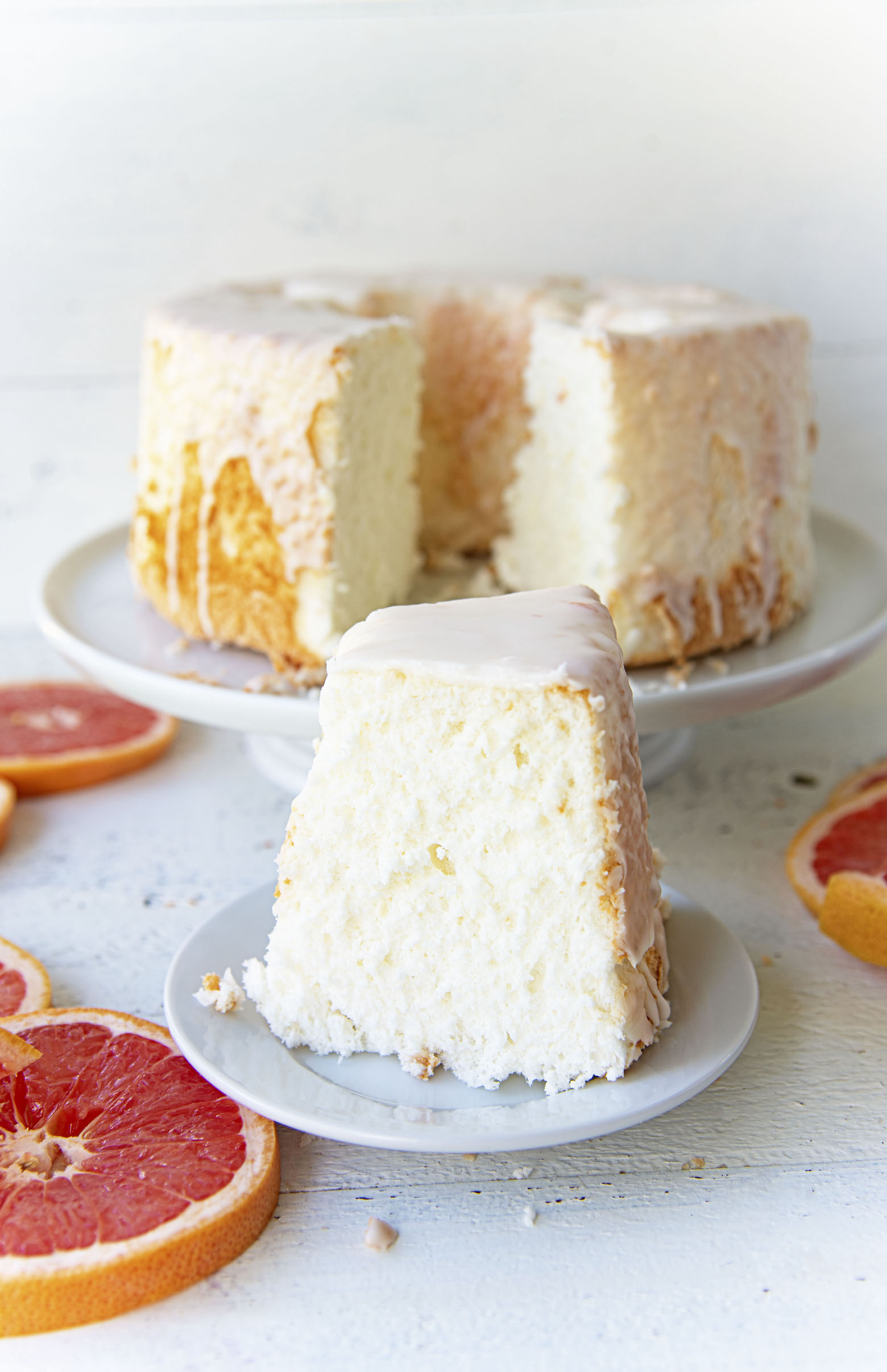 Side view of slice of Ruby Red Grapefruit Glazed Angel Food Cake with cake in background.