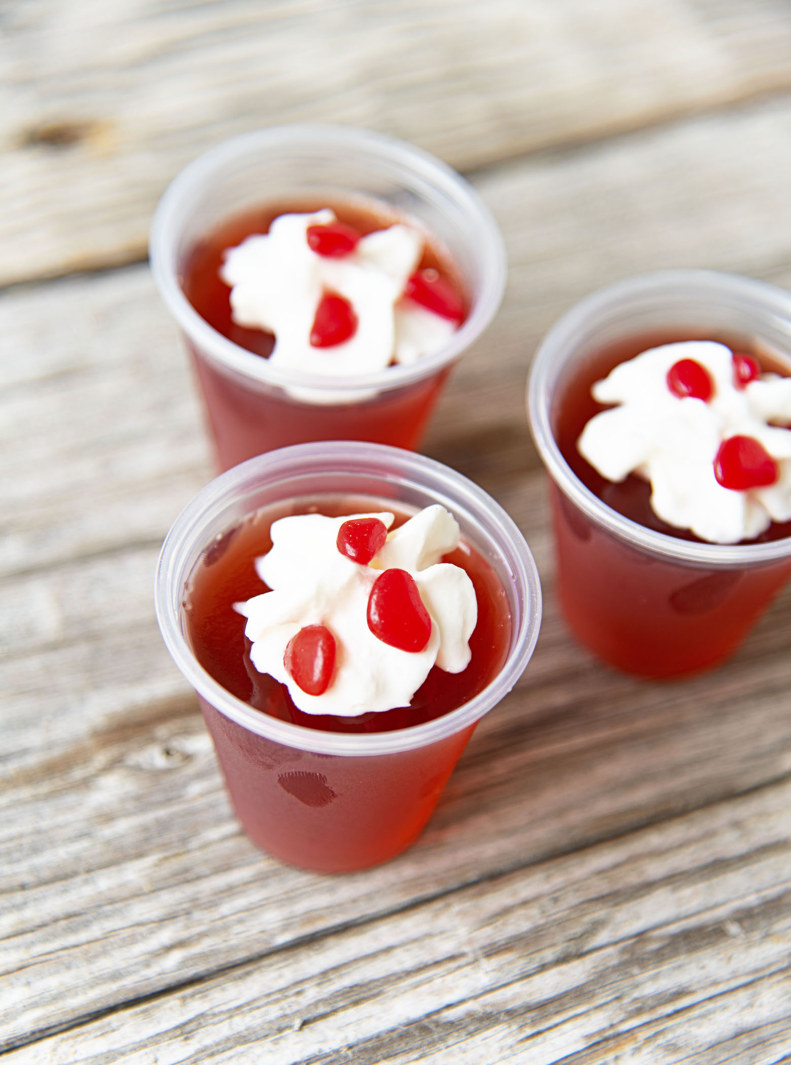 Three Cinnamon Candied Apple Jello Shots gathered together topped with whipped cream and cinnamon red hots candies.