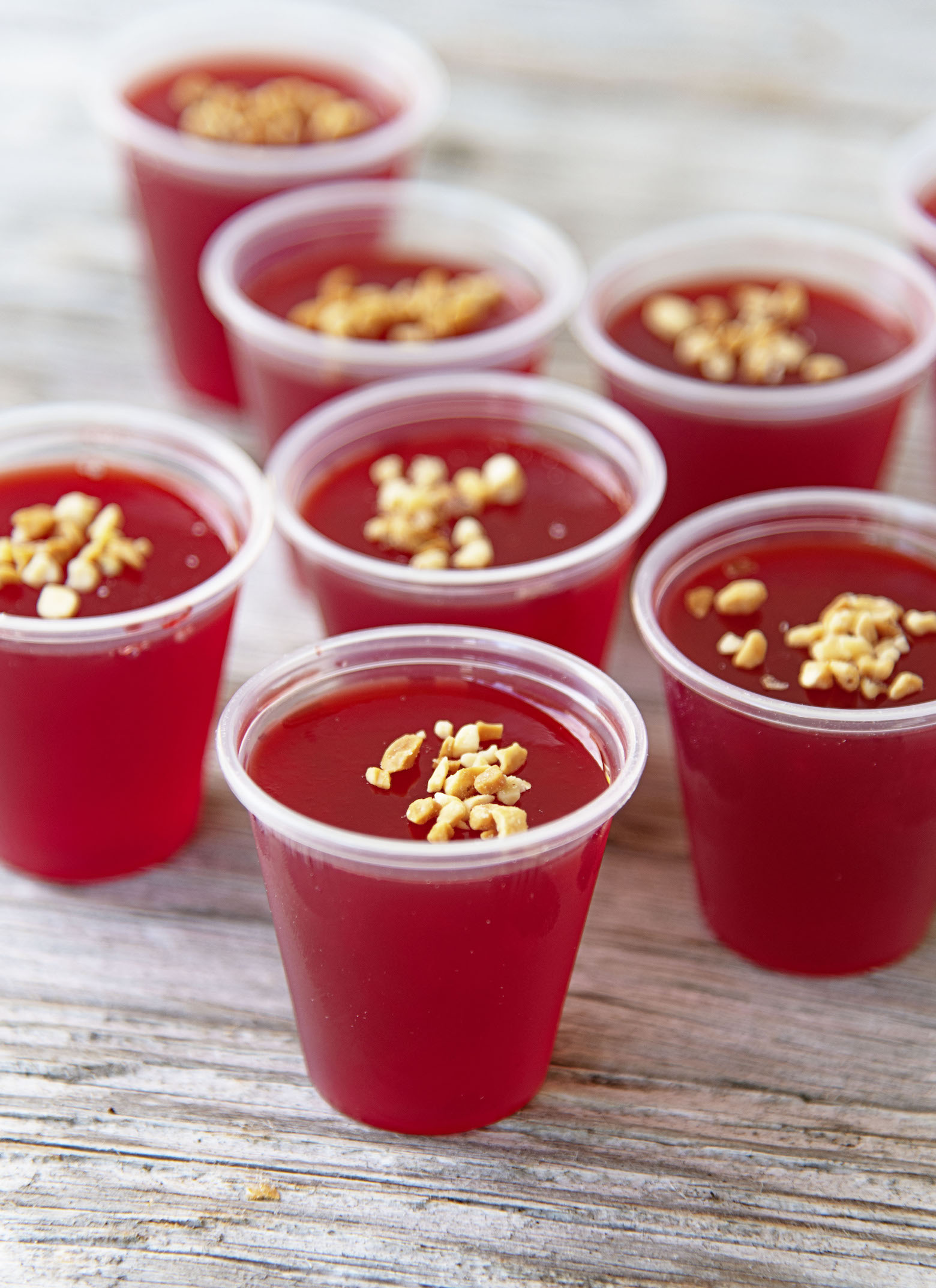 A bunch of Peanut Butter Raspberry Jello Shots gathered with chopped peanuts as garnish on top of them. 