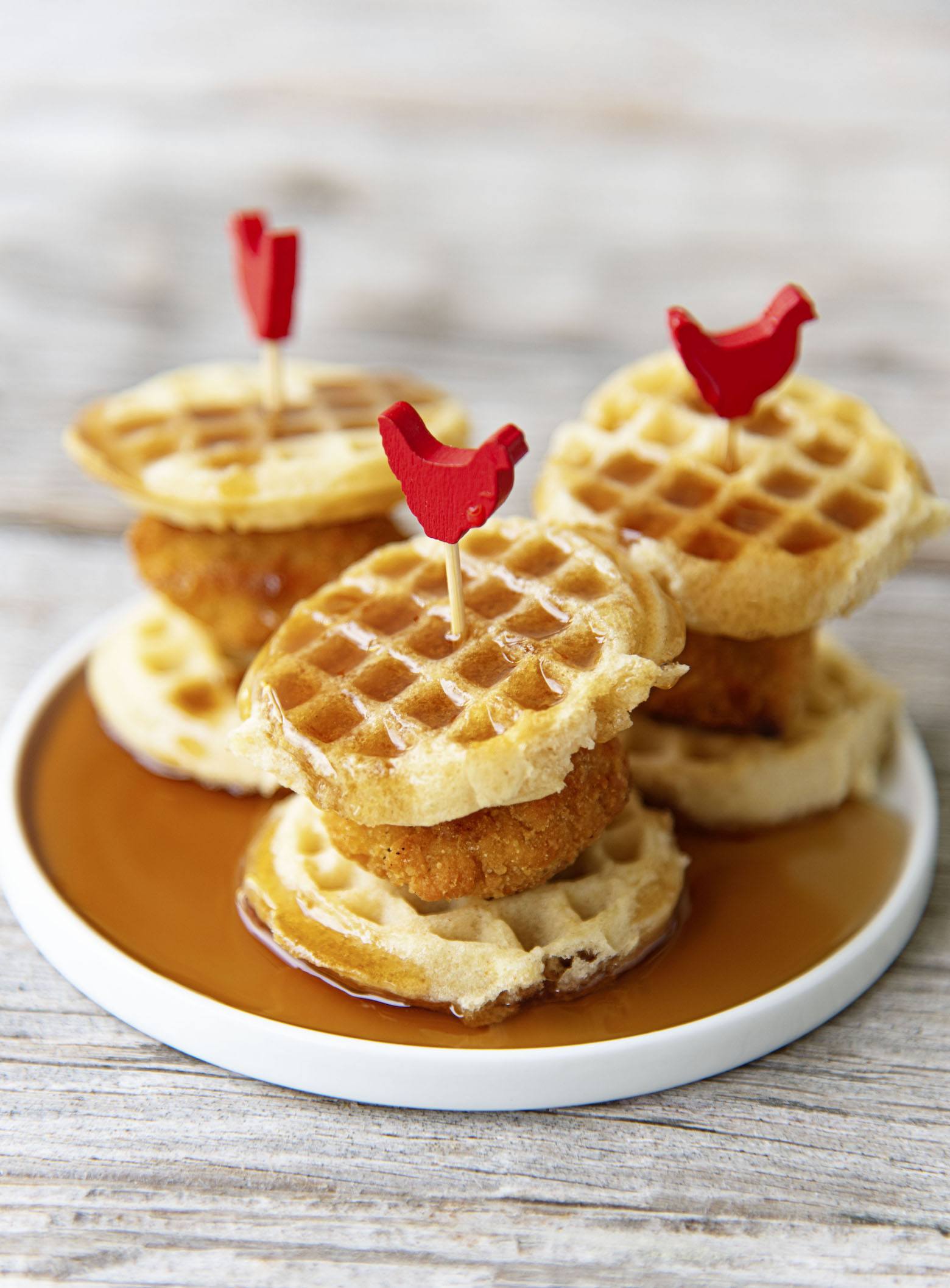 Side view of three Mini Chick’n and Waffles on a small plate covered in syrup. 