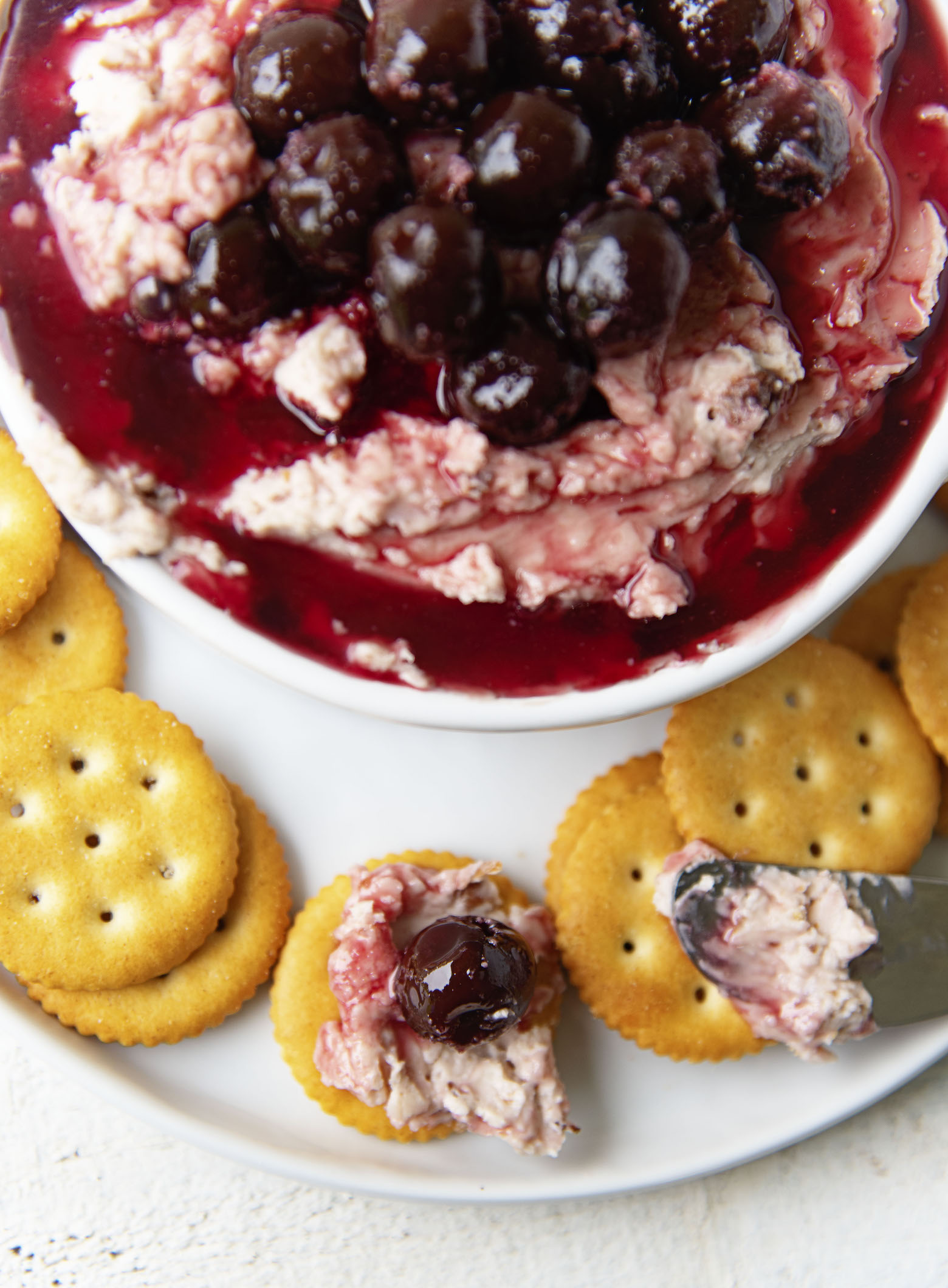 Overhead view of Cherry Cheddar Cheese Spread with one cracker covered with the spread and a cherry. 