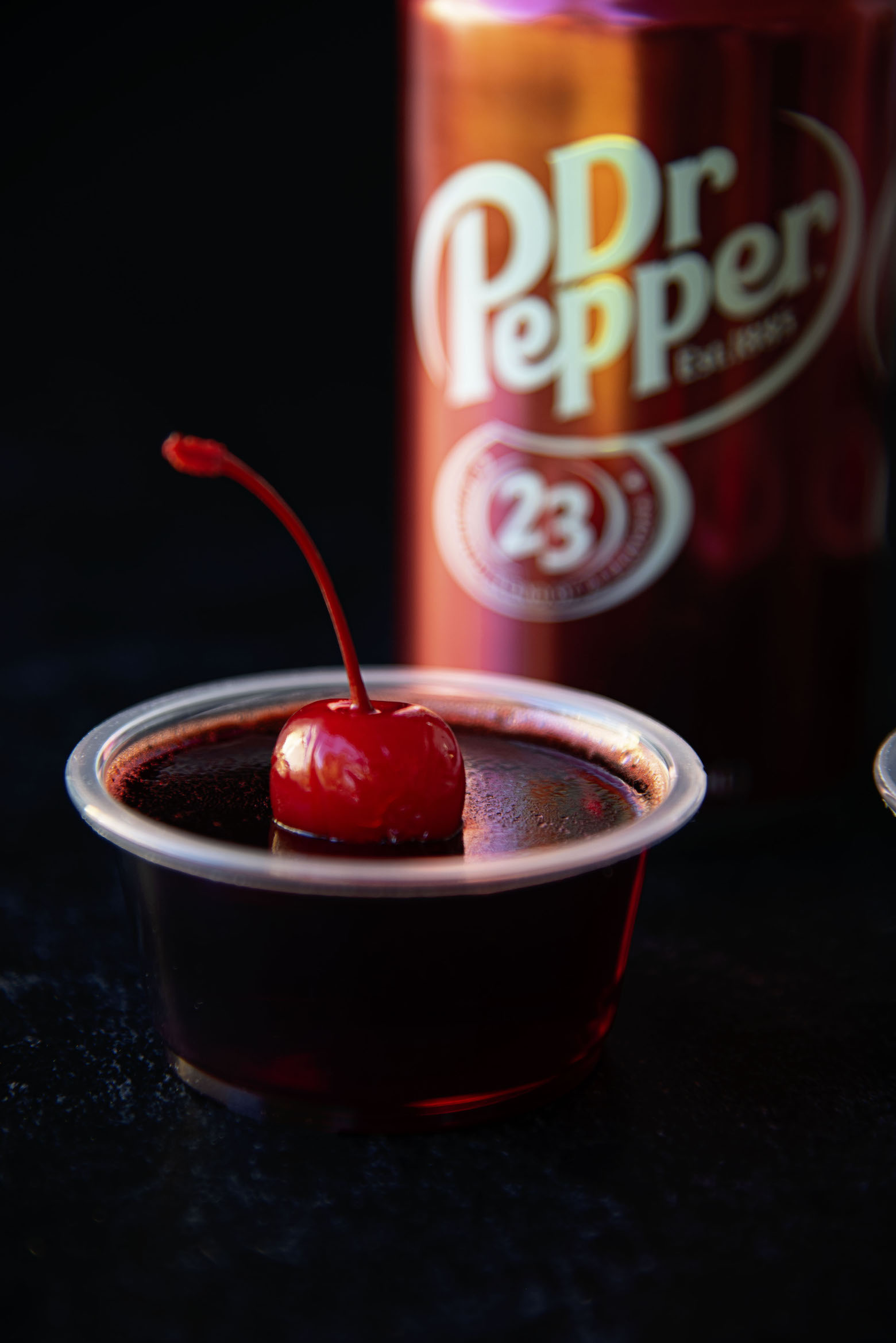 Single Jello Shot with Dr. Pepper can in background.