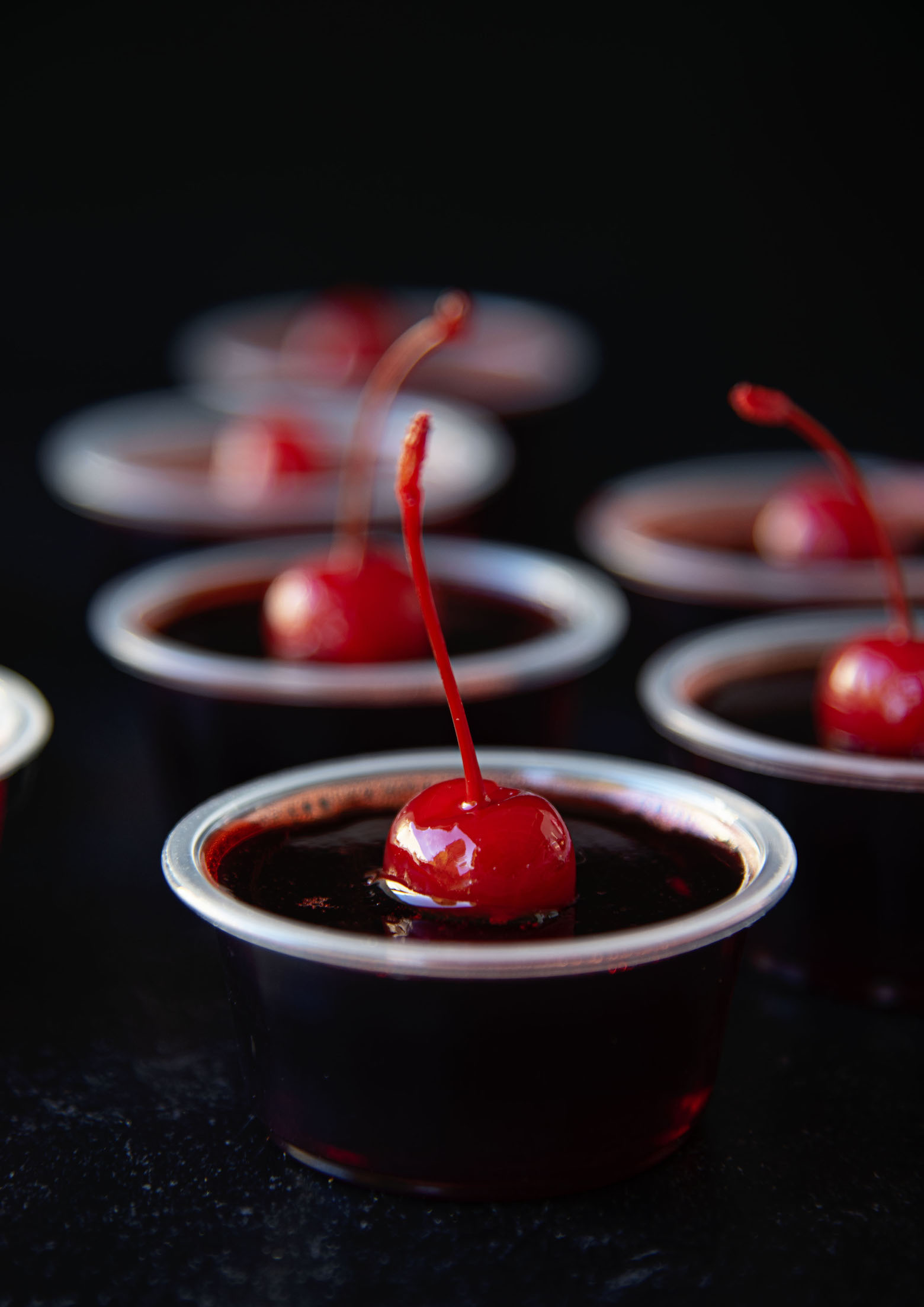 Side view of Cherry Fire Pepper Jello Shots with stemmed cherries coming out of the shot. 