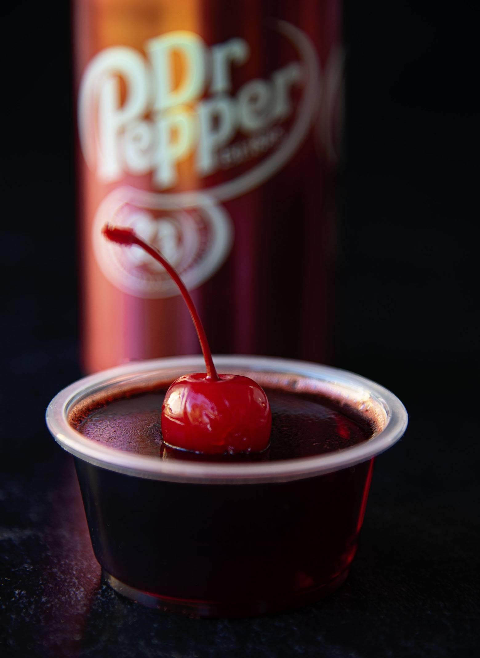 Front view of single cherry fire pepper jello shot with Dr. Pepper can in background. 