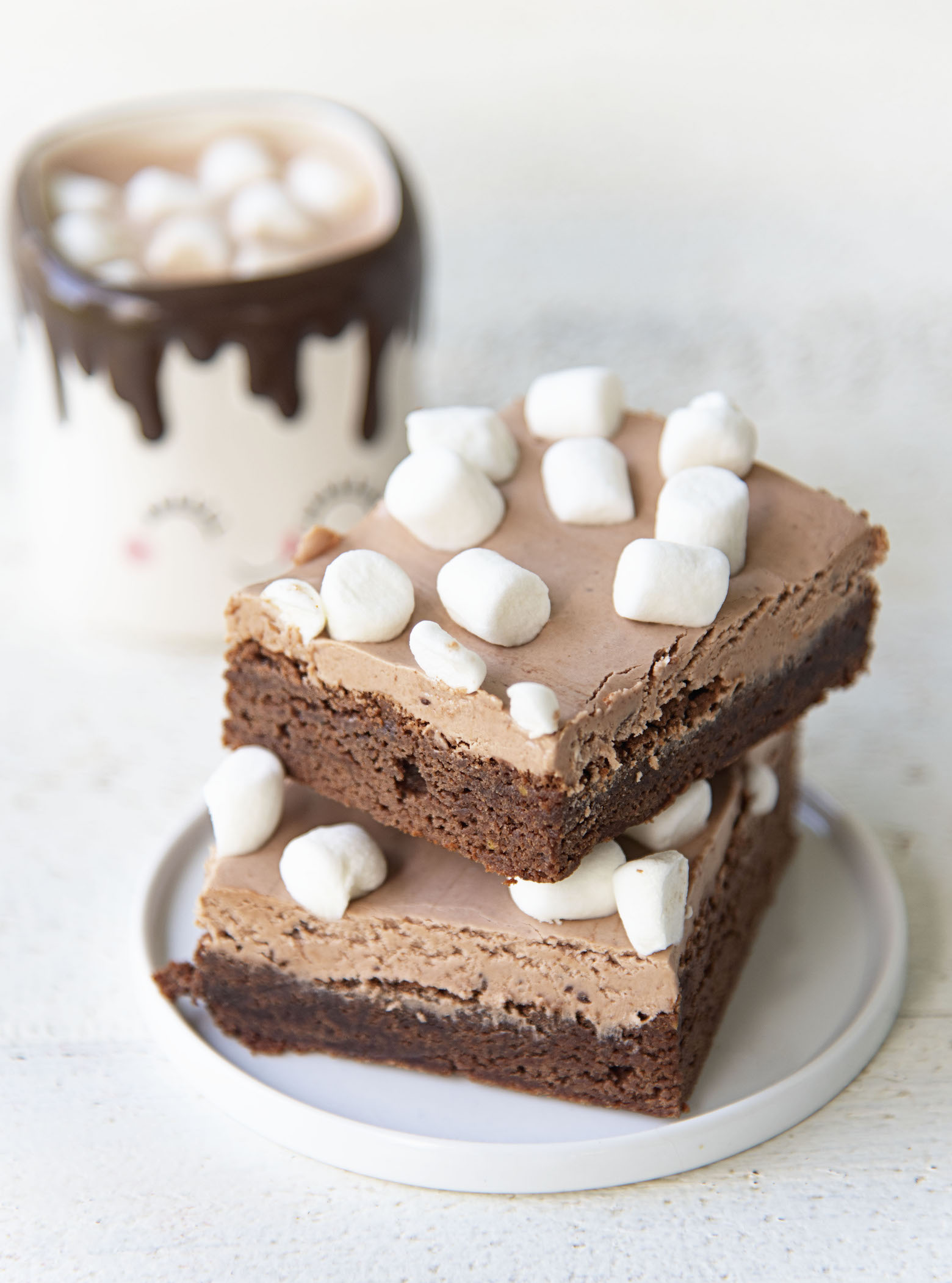 Two stacked hot chocolate brownies on a plate with a cup of hot chocolate in the background. 