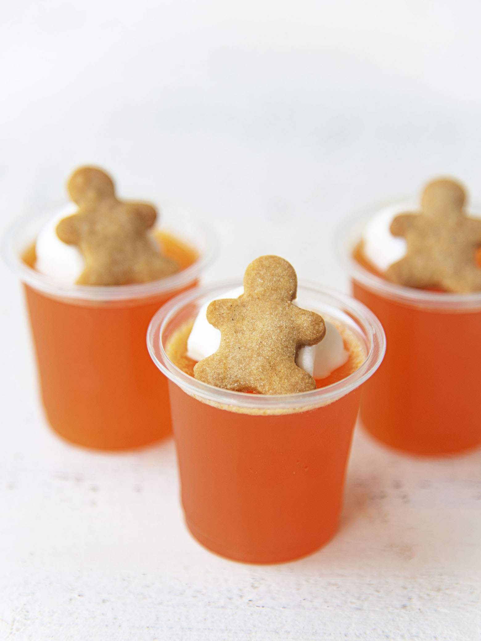 Three Orange Gingerbread Jello Shots with a close up of the gingerbread man cookie on top of the shot.